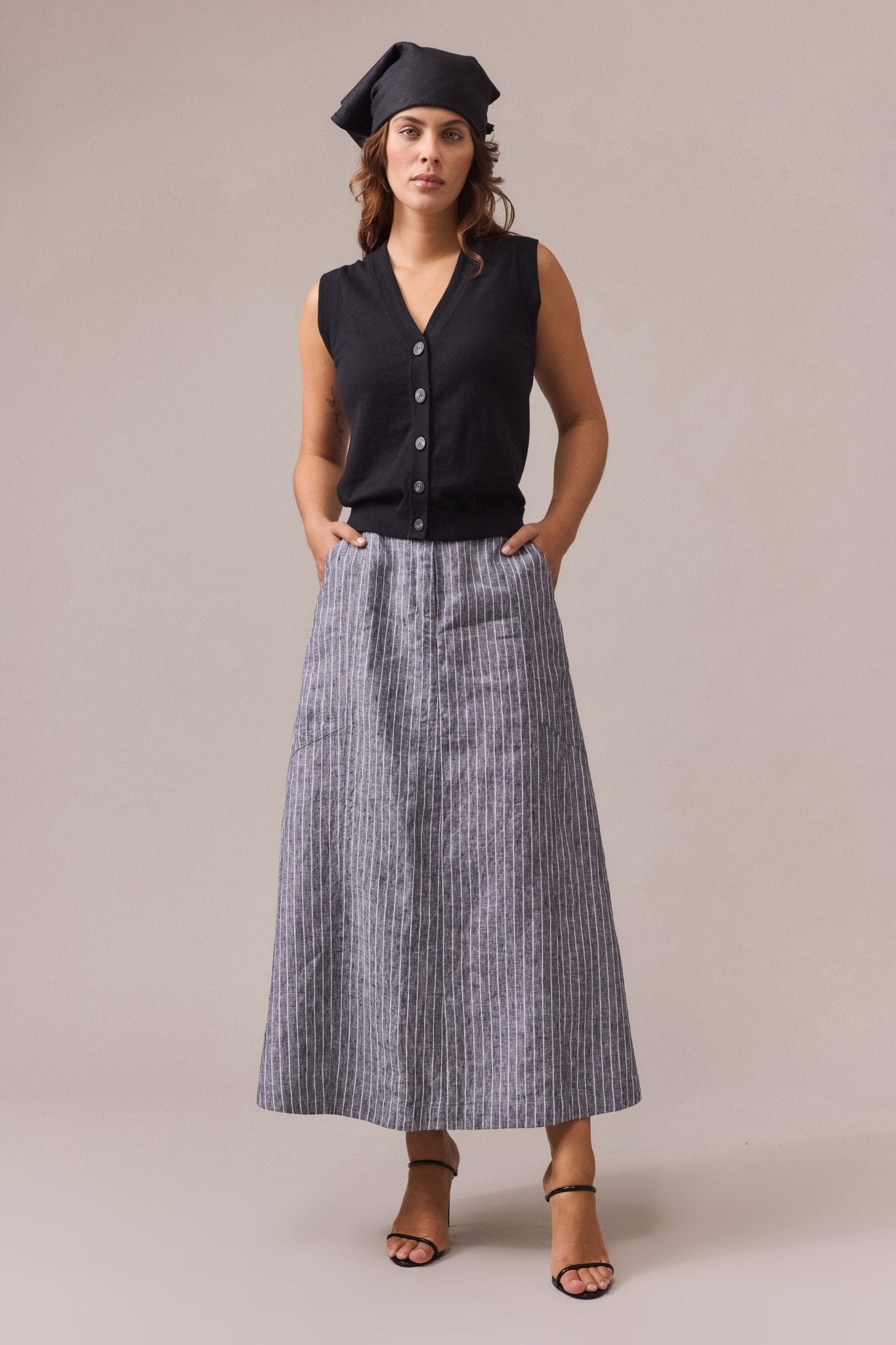 a woman wearing a black button-up cotton cashmere vest, paired with a striped maxi linen skirt