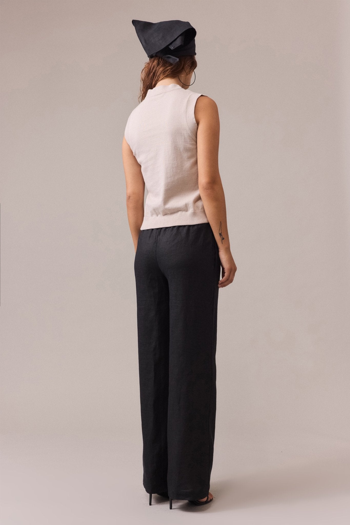 A woman seen from the back, wearing a women's sand cotton cashmere vest, paired with a black pant.