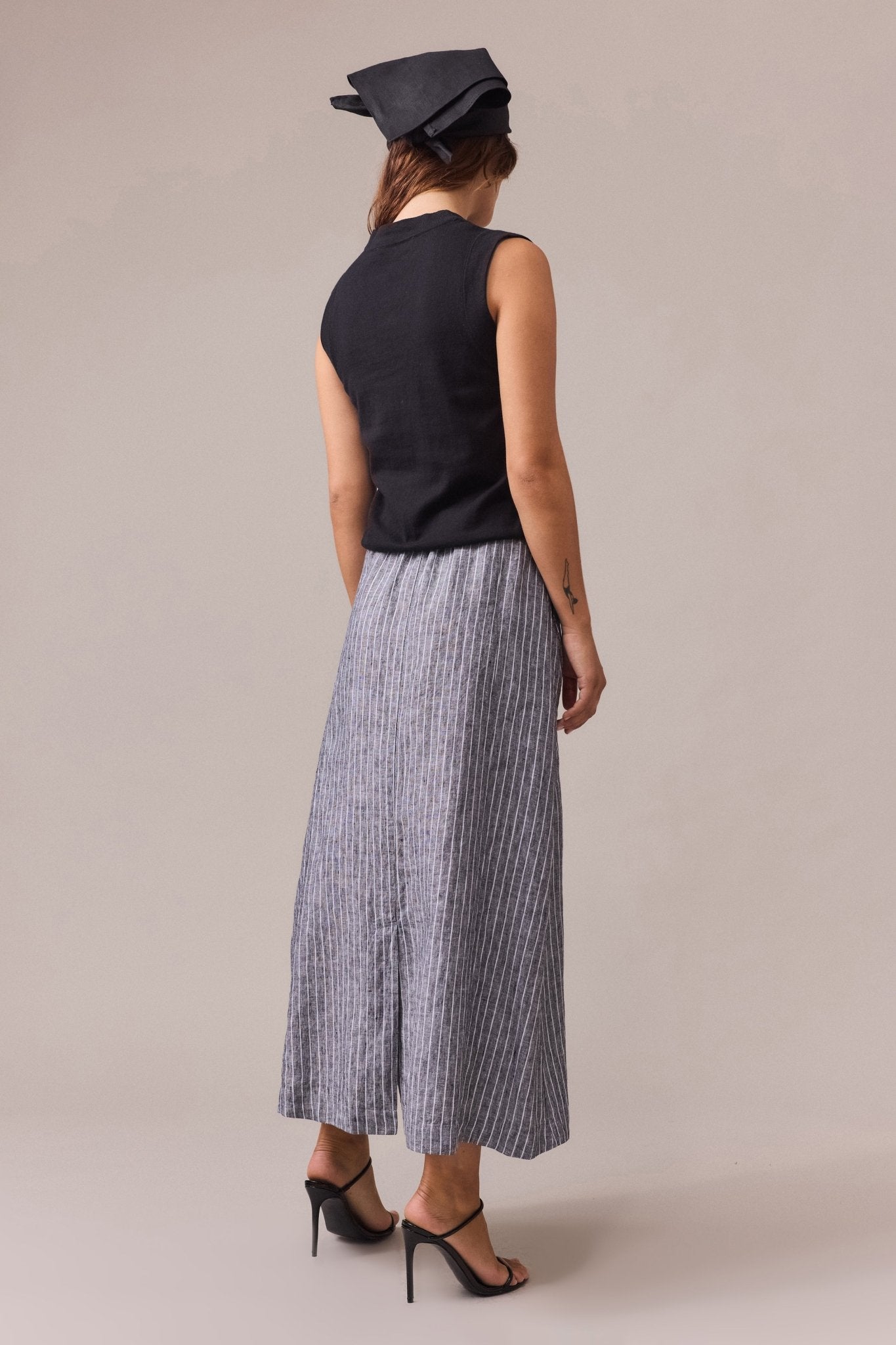 a woman seen from the back, wearing a women's black cotton cashmere vest, paired with a striped maxi linen skirt