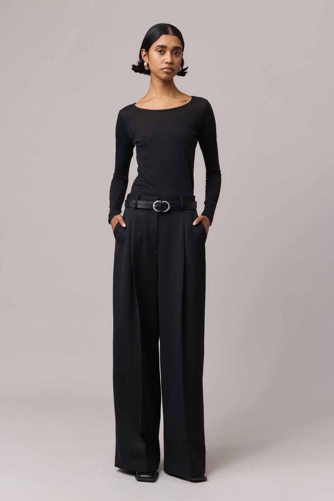 Woman wearing a black featherlight 100% cotton long-sleeve top with a crew neck, styled with high-waisted black trousers and a belt.