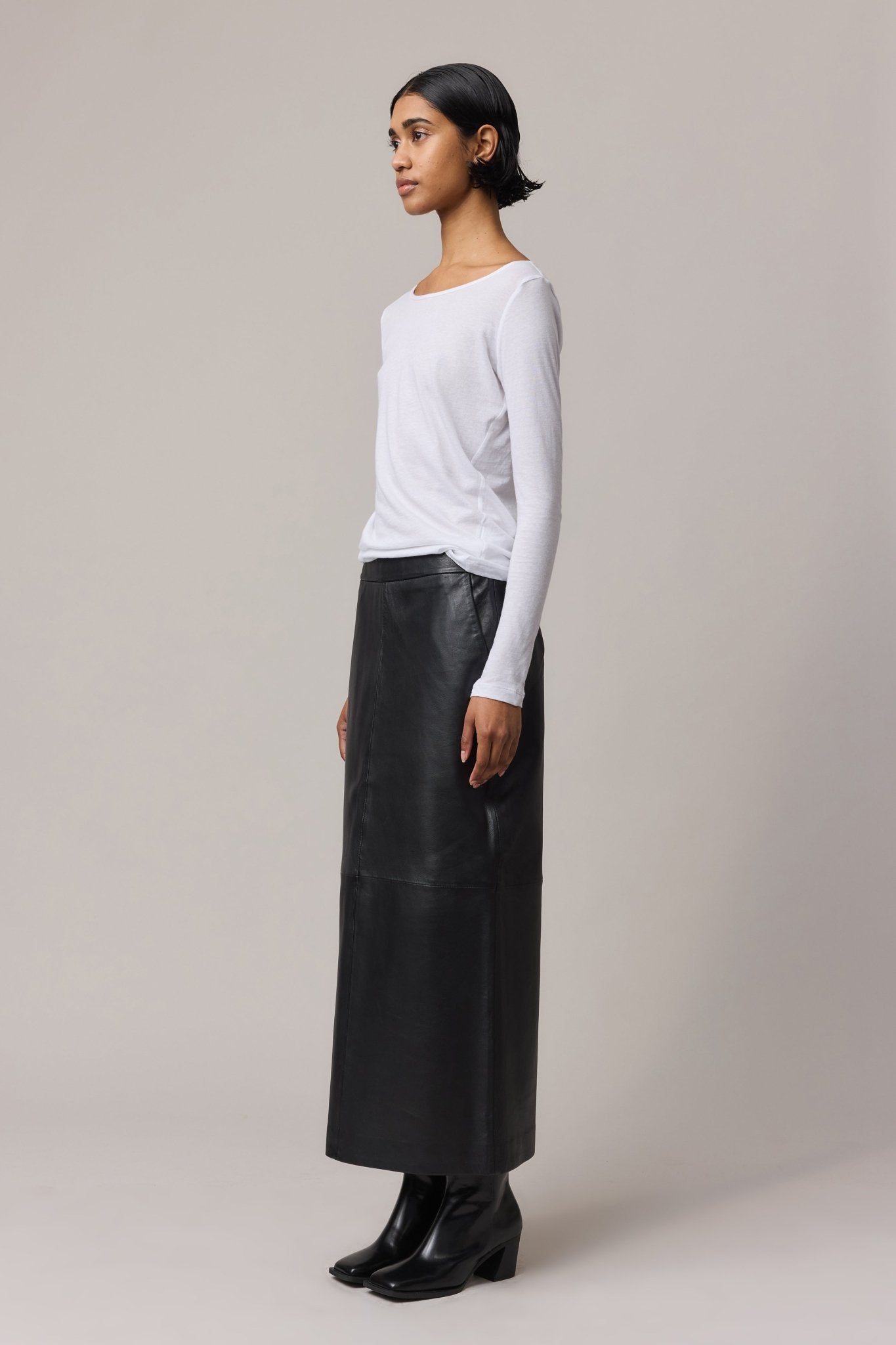 Side view of the woman in a semi-sheer white top, styled effortlessly with a leather skirt.