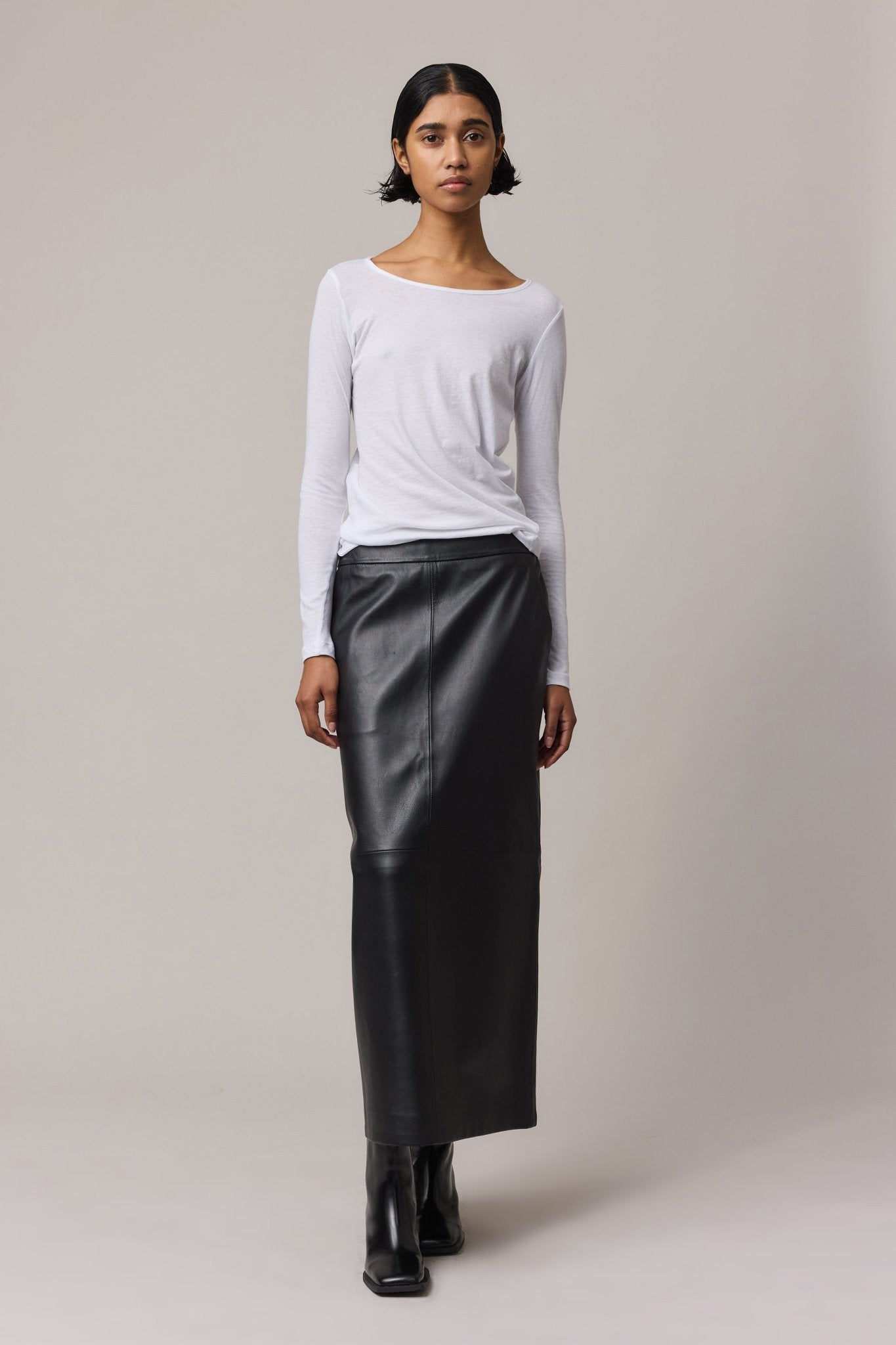 Woman wearing a white cotton long-sleeve top with a crew neck, paired with a black leather skirt.