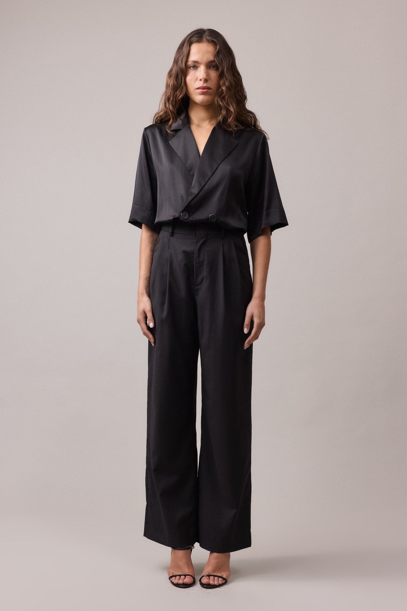 Woman wearing the black Frankie Wide Leg Pant, paired with a black shirt. The high-waist, wide-leg fit of the pants creates a relaxed, and flattering silhouette.