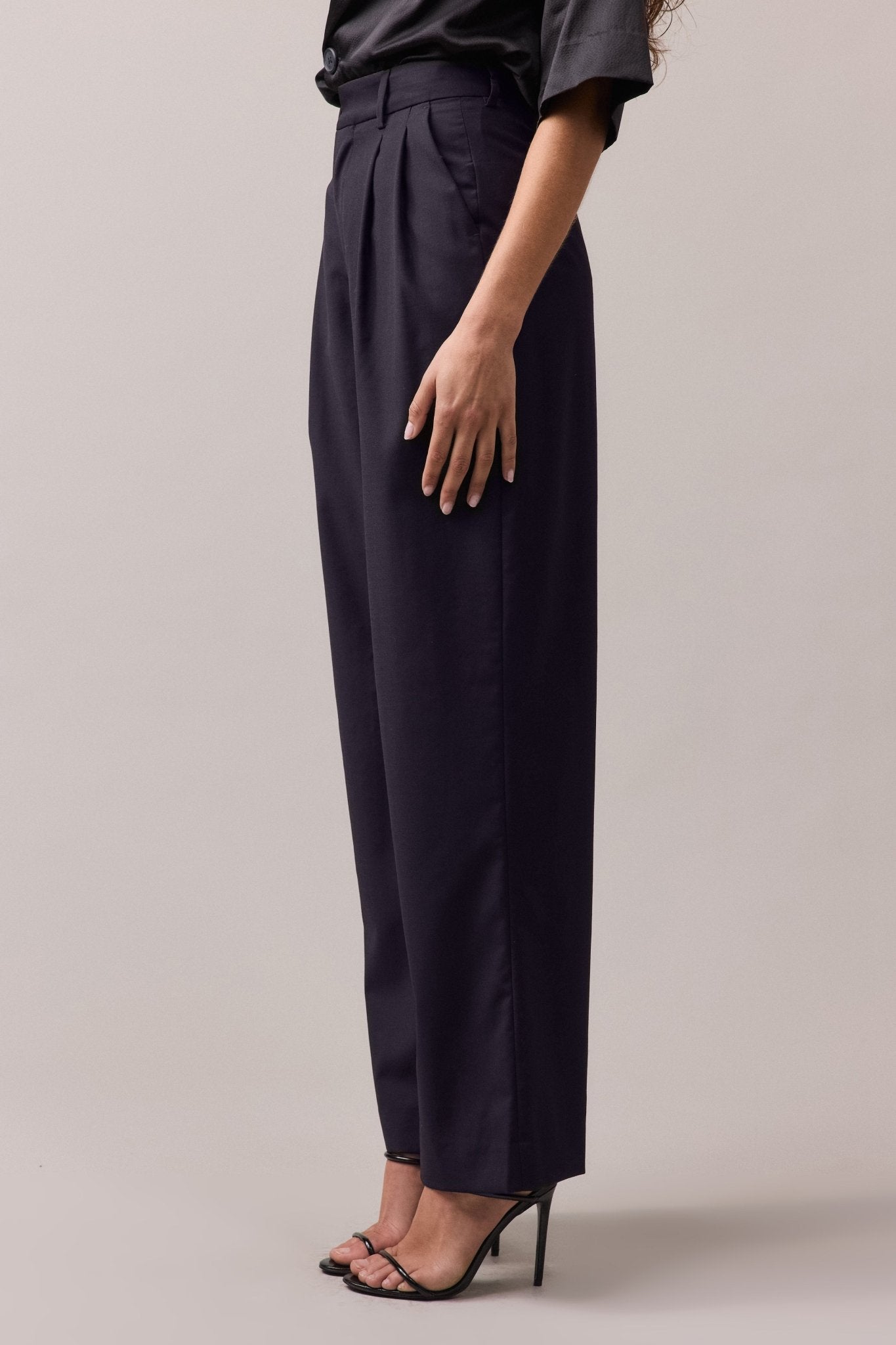 Side view of the woman wearing the Frankie Wide Leg wool pant. The pants feature a high to mid waist, wide-leg fit, and double front pleat, highlighting the relaxed and flattering silhouette.