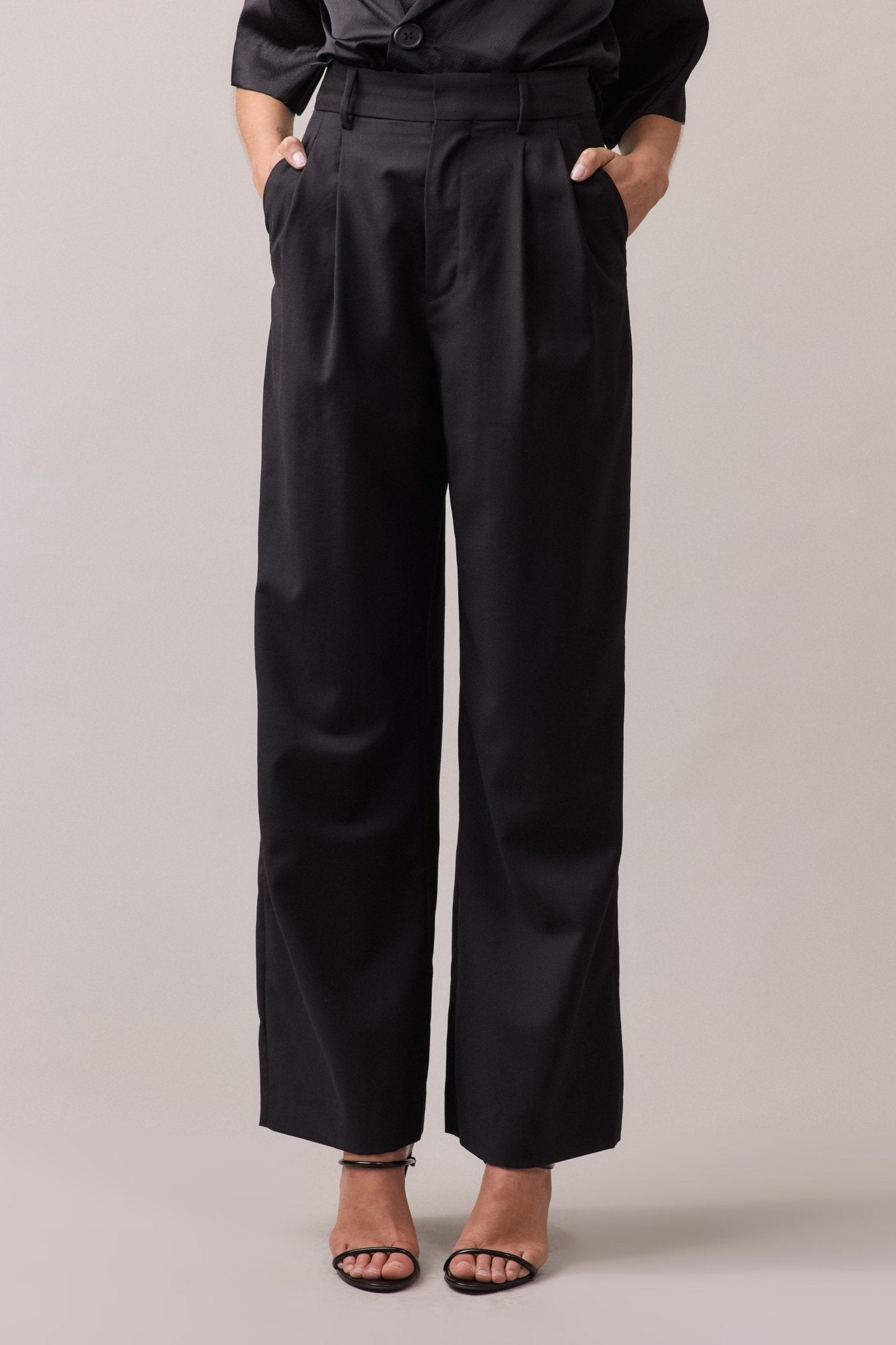 Woman wearing the black Frankie Wide Leg Pant in 100% wool, with her hands in the front side seam pockets. 