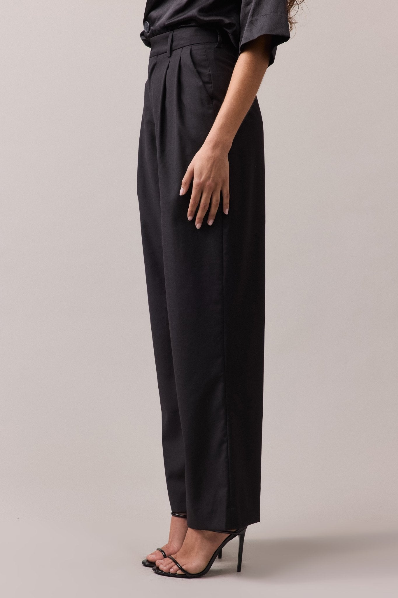 Side view of the woman wearing the black Frankie Wide Leg Pant. The high waist, wide-leg fit, and double front pleat are visible, highlighting the relaxed, flattering silhouette.