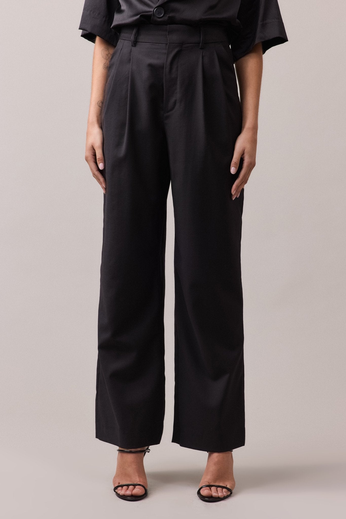 Woman wearing the black Frankie Wide Leg Pant in 100% wool, showcasing the high waist and wide-leg fit. The pants feature side seam pockets, back jet pockets, a double front pleat, and belt loops.