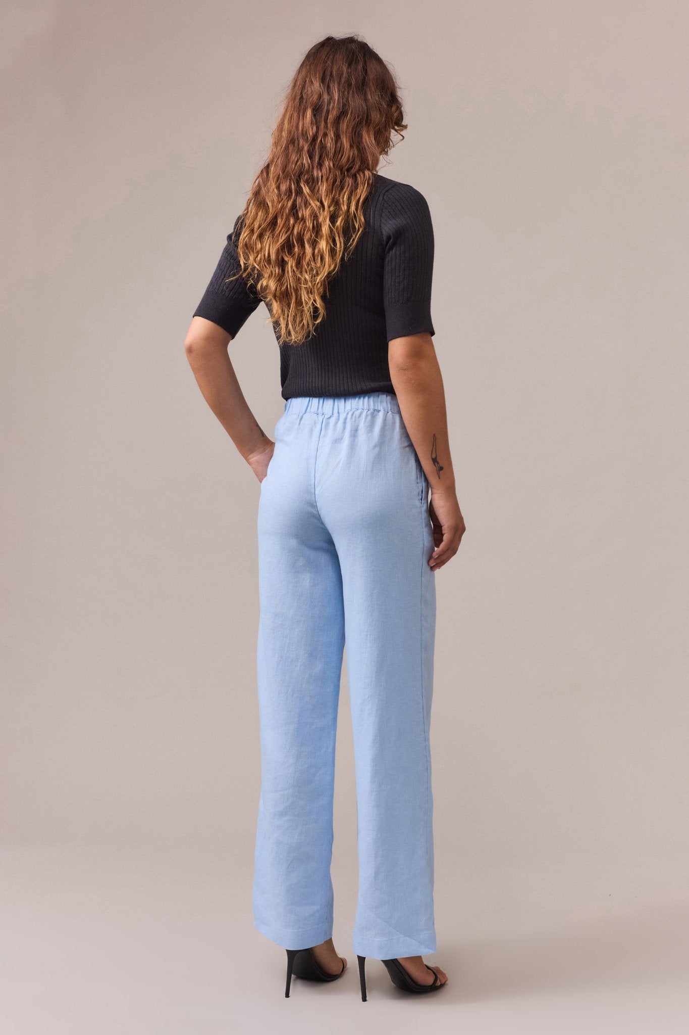 a woman seen from the back, wearing pale blue linen pants paired with a black shirt