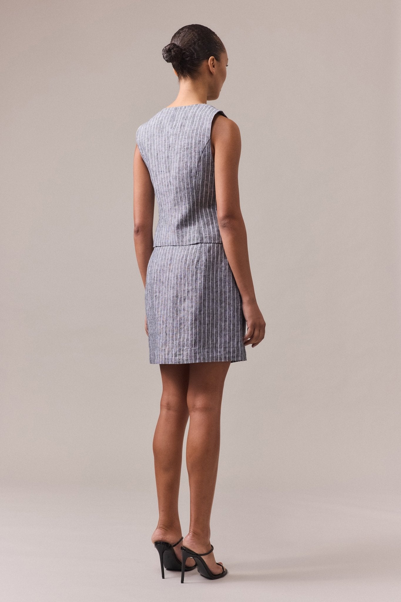 A woman seen from the back, wearing a black striped linen A-line skirt paired with a vest.