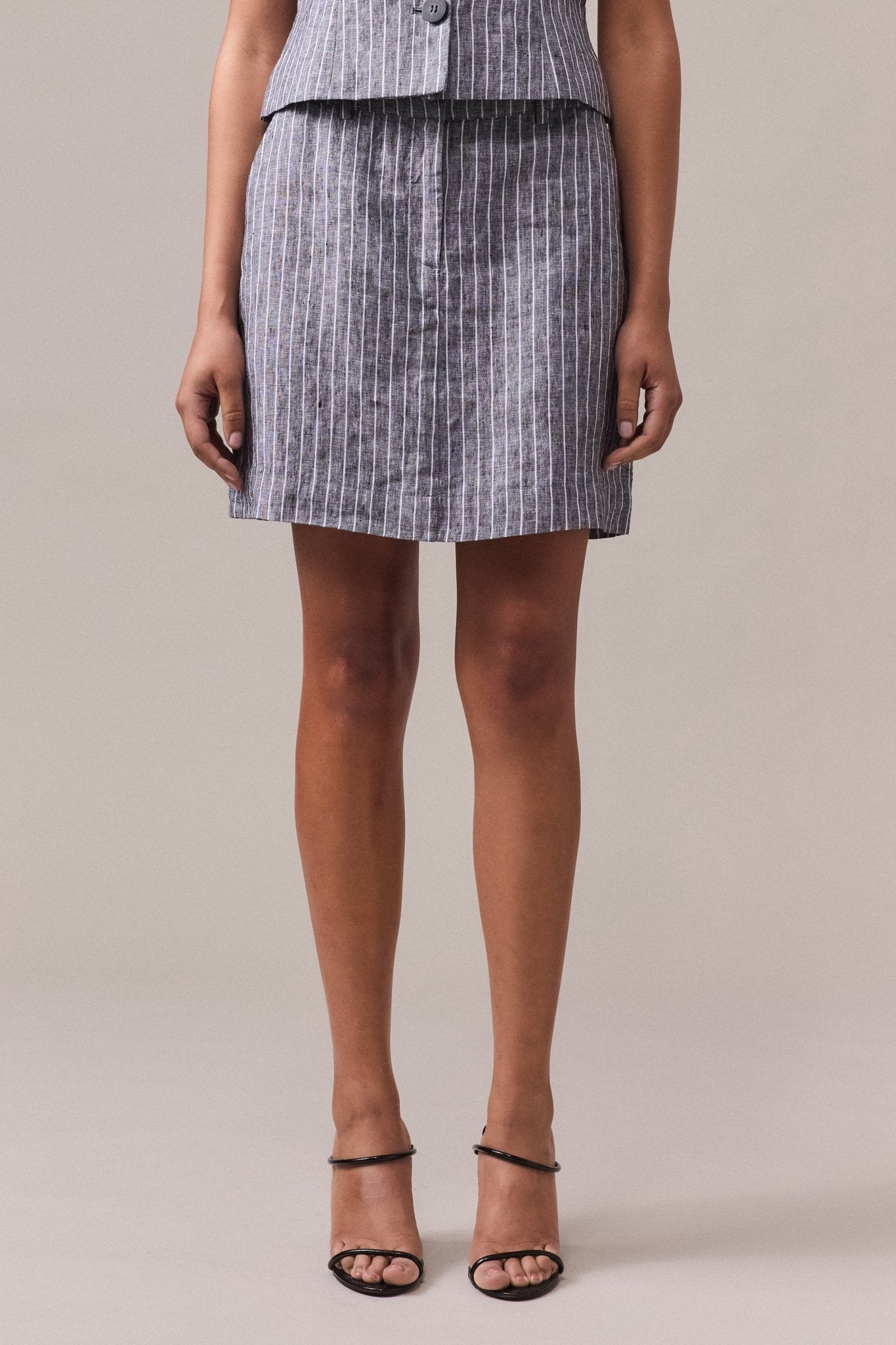 A woman wearing a striped linen A-line skirt with a fixed waistband, side seam pockets, and a short above-the-knee length.