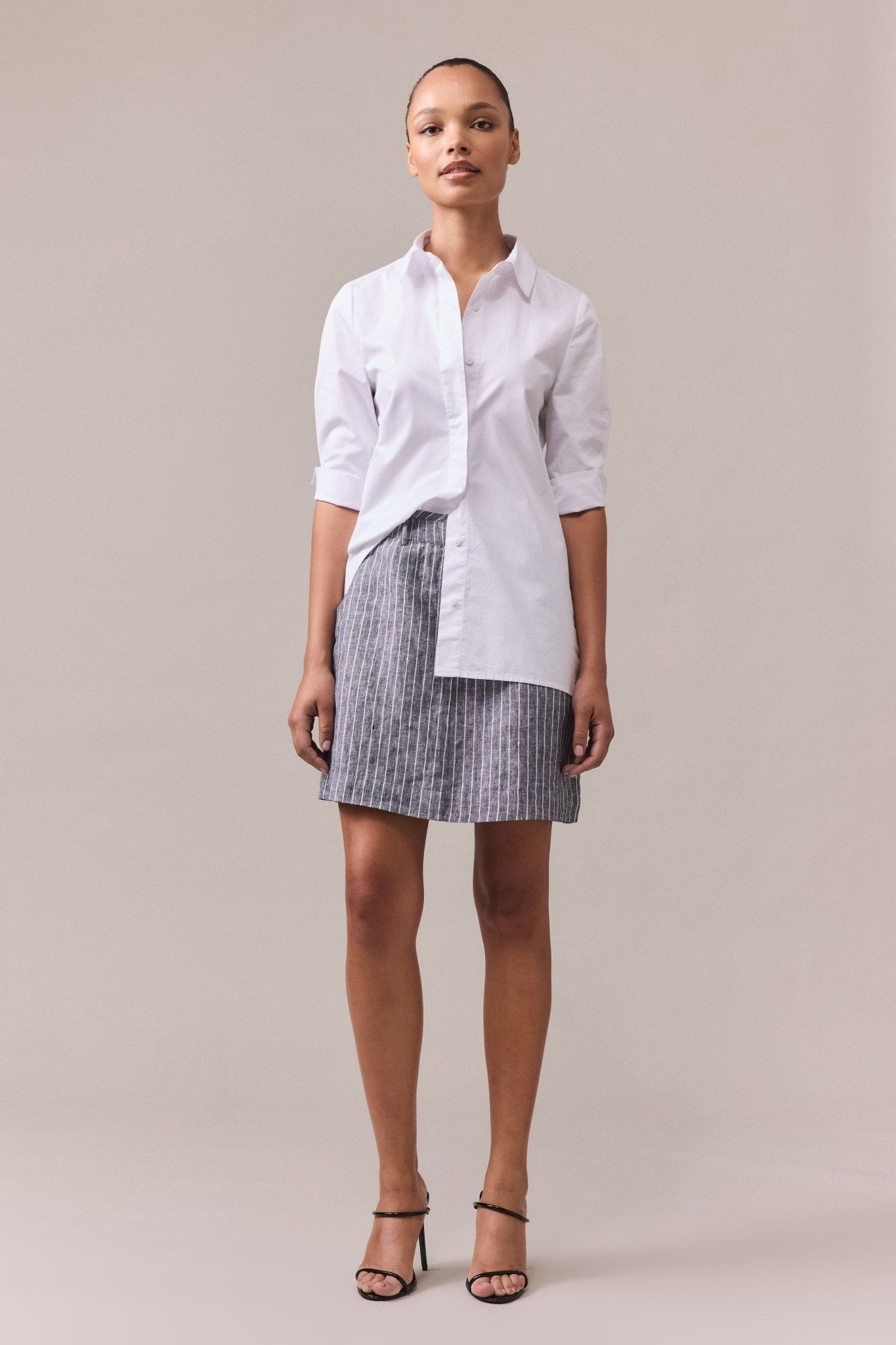 A woman wearing a black striped linen A-line skirt paired with a white shirt.