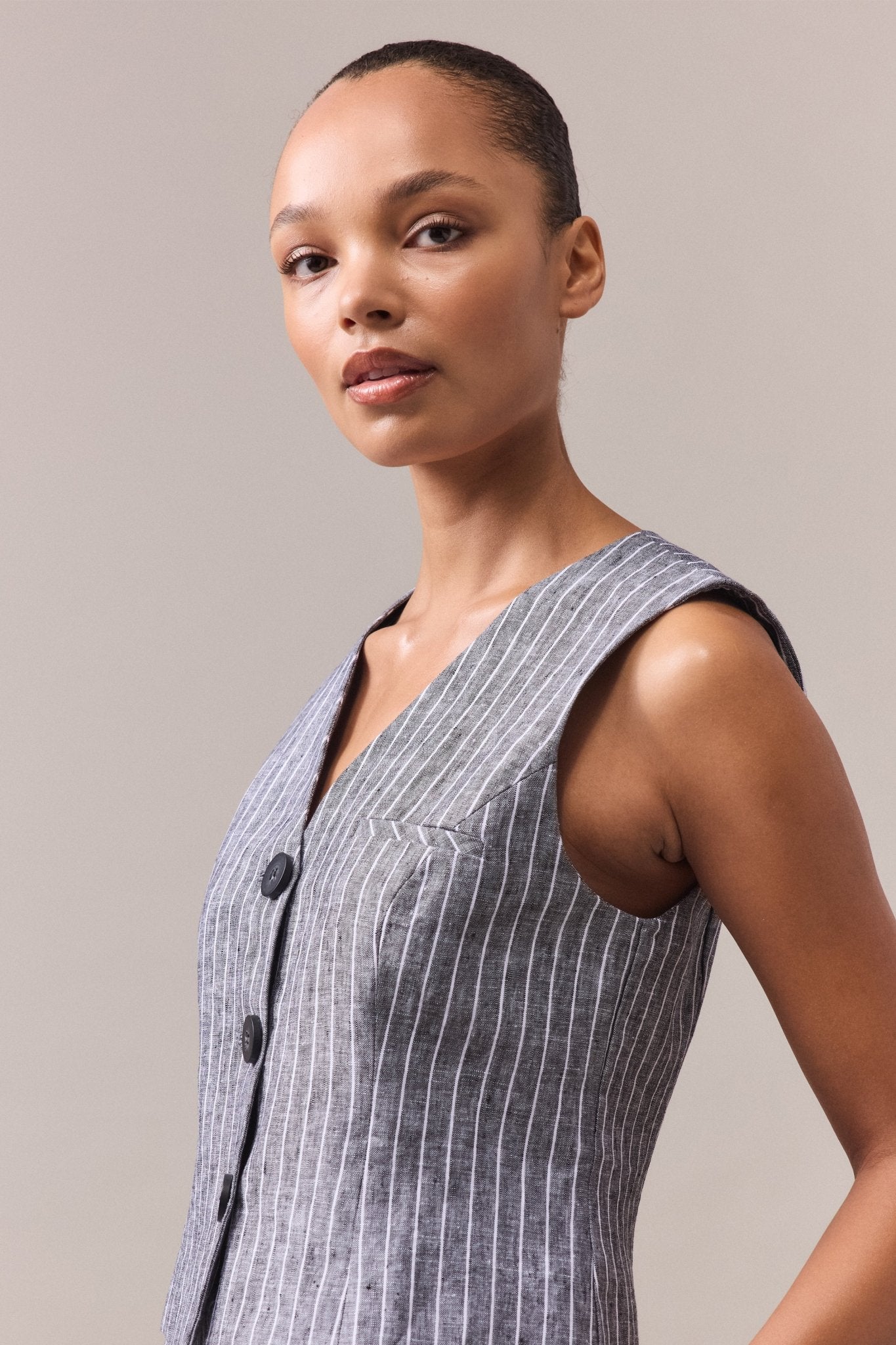 Women is wearing grey linen vest with white stripes and grey buttons.