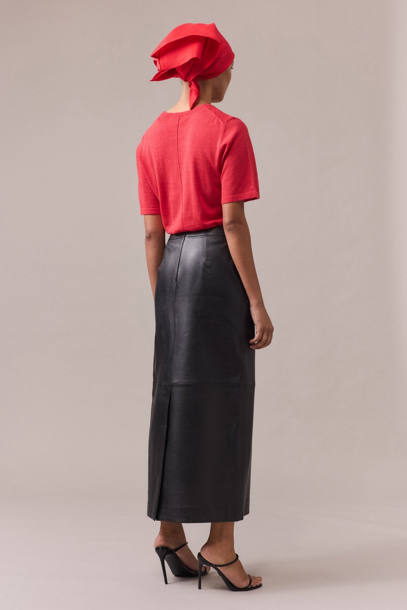 Back view of a woman wearing the Kara leather pencil skirt with a red tee, showcasing the sleek silhouette of the skirt and its flattering fit.