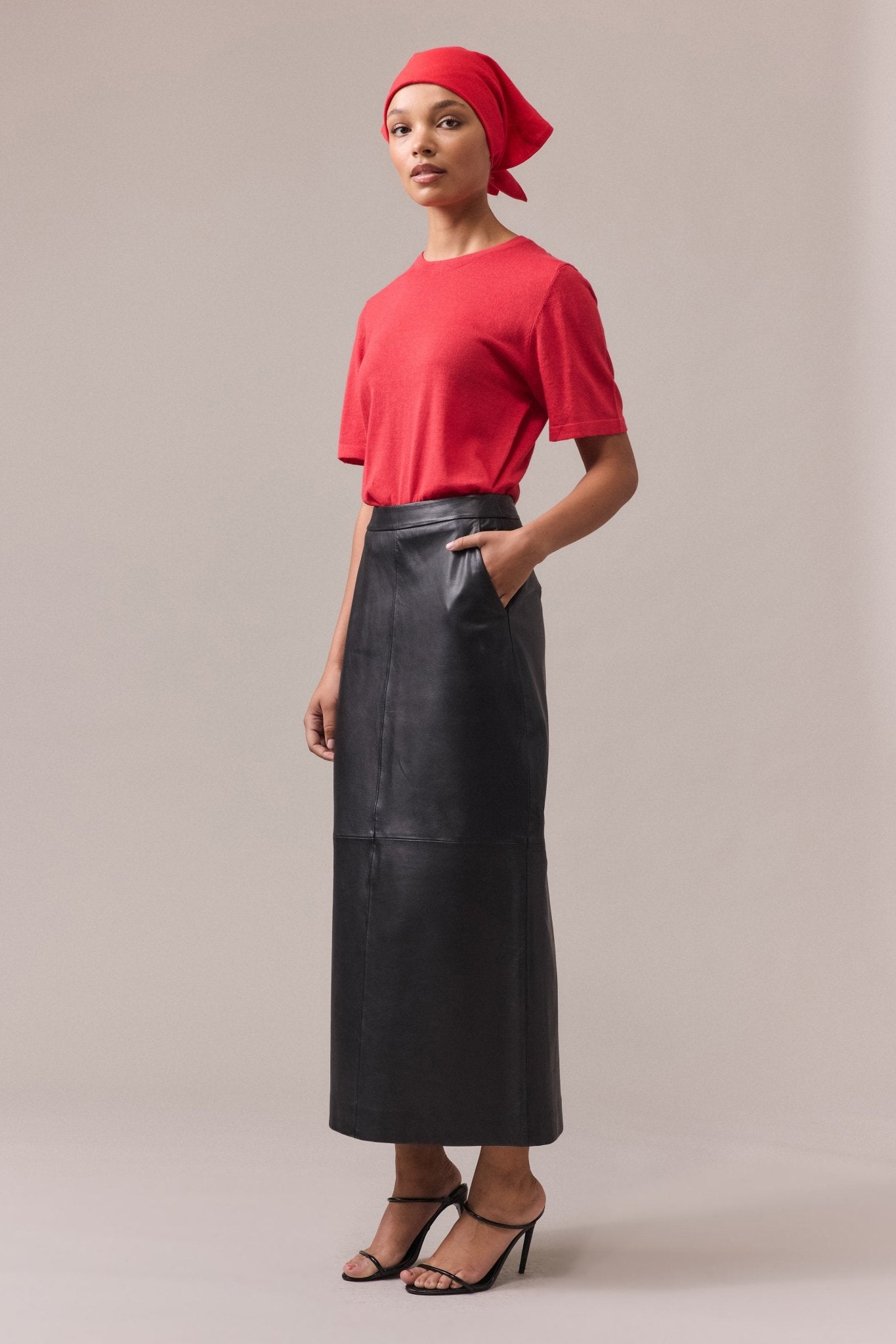 Side view of a woman wearing the Kara leather pencil skirt with a red tee, one hand casually tucked into the skirt pocket, highlighting the relaxed yet stylish look.