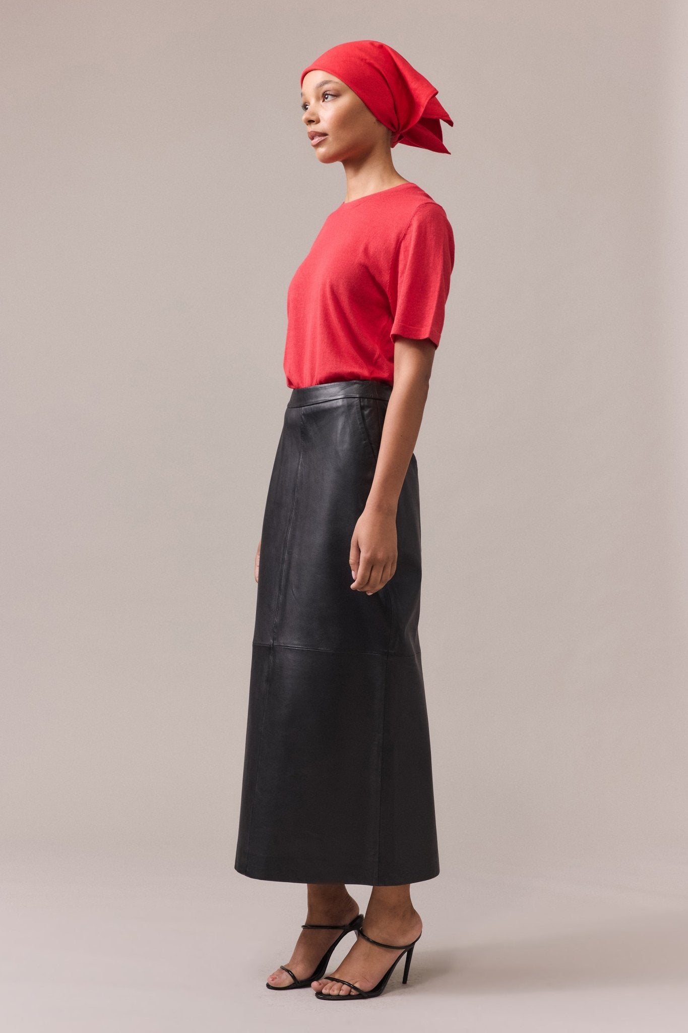 Side view of a woman wearing the Kara leather pencil skirt paired with a red tee, showcasing the sleek silhouette of the skirt and the casual styling of the top.