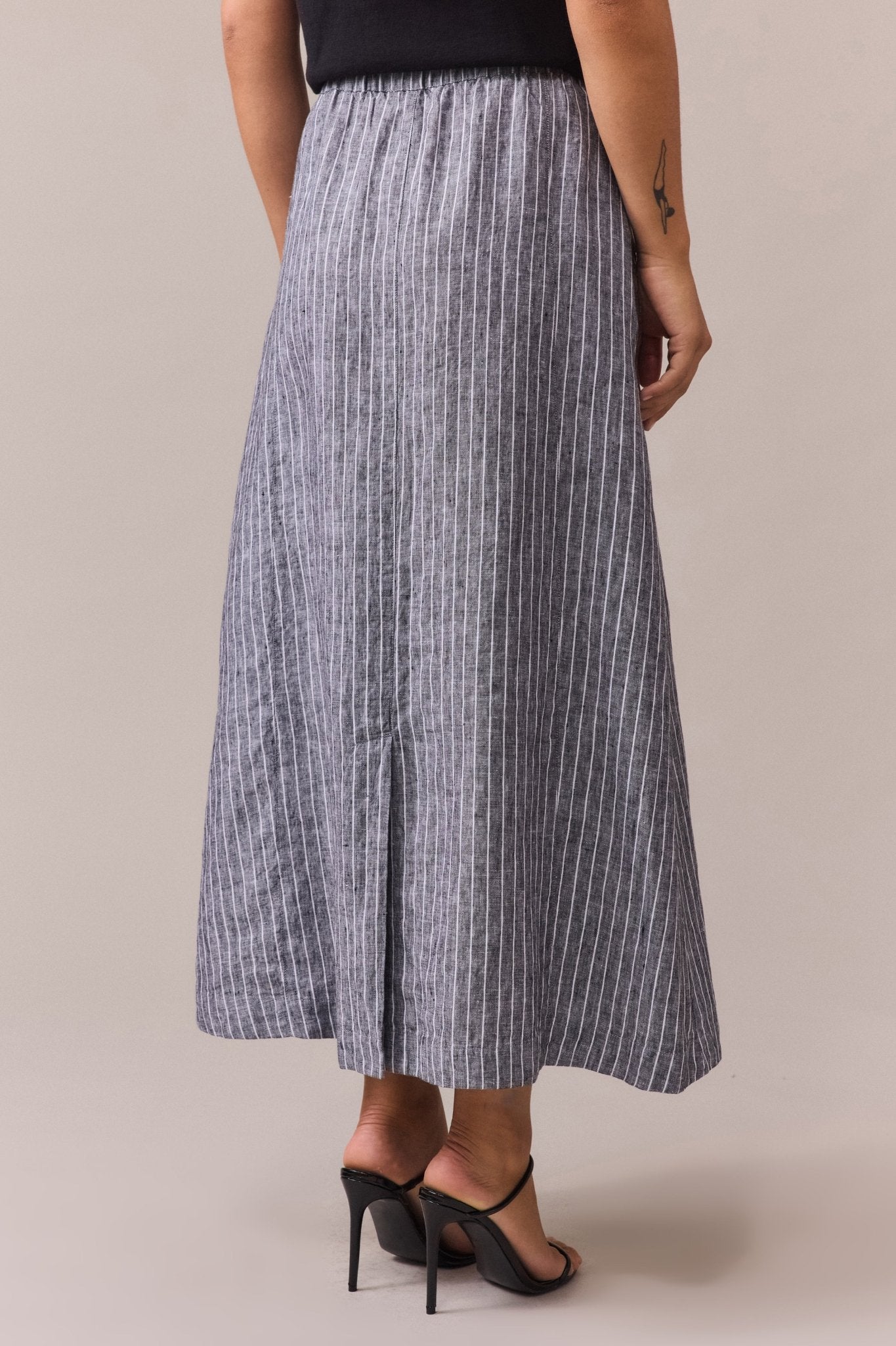 a woman from the back, wearing a high-waisted, striped maxi linen skirt with vertical white stripes on a gray fabric