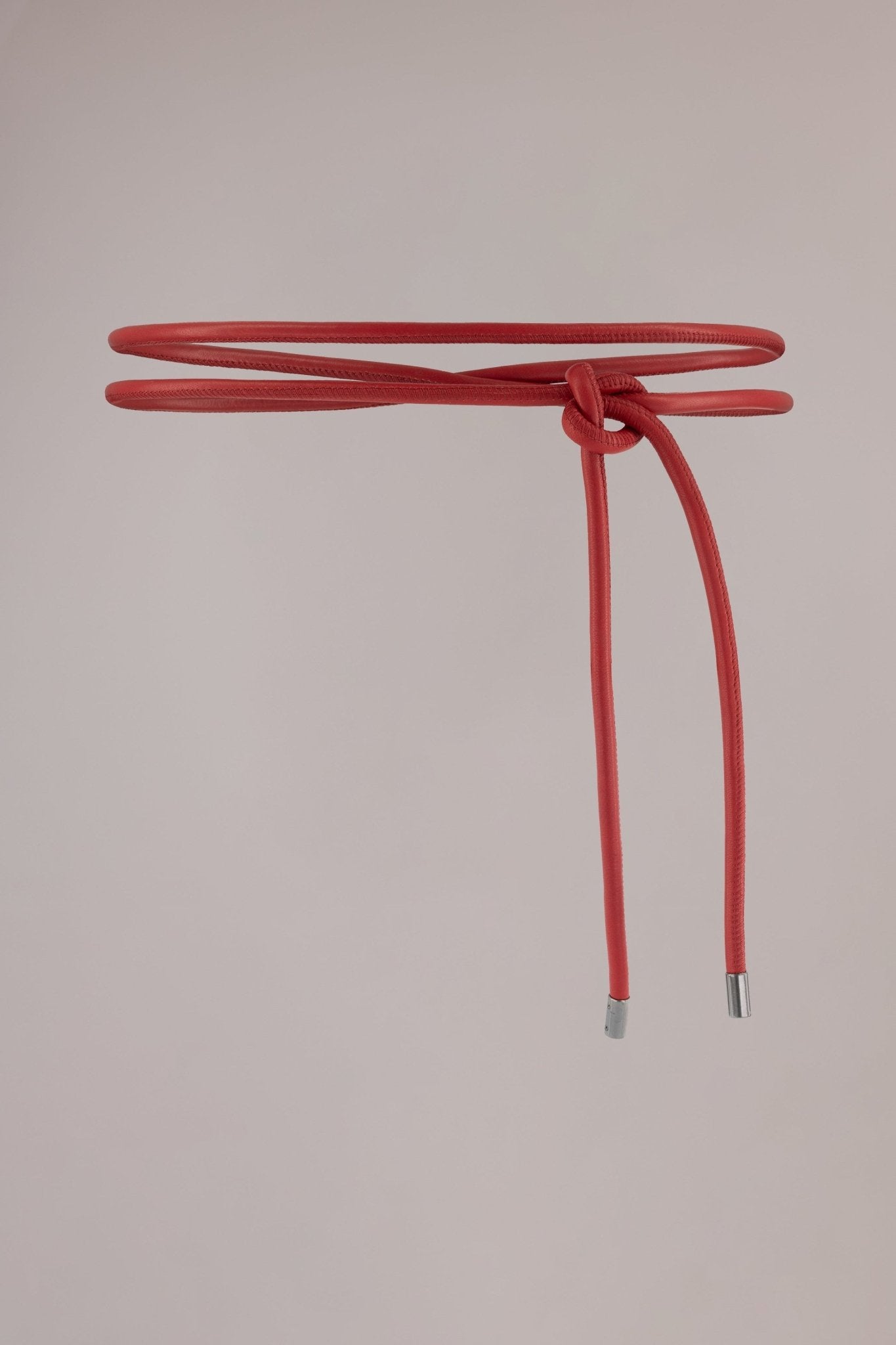 Red leather wrap belt made from soft, premium leather with whipstitch detailing and sleek gunmetal metal cylinder ends. Designed to be wrapped and tied around the waist twice, this belt adds a bold statement to any outfit.