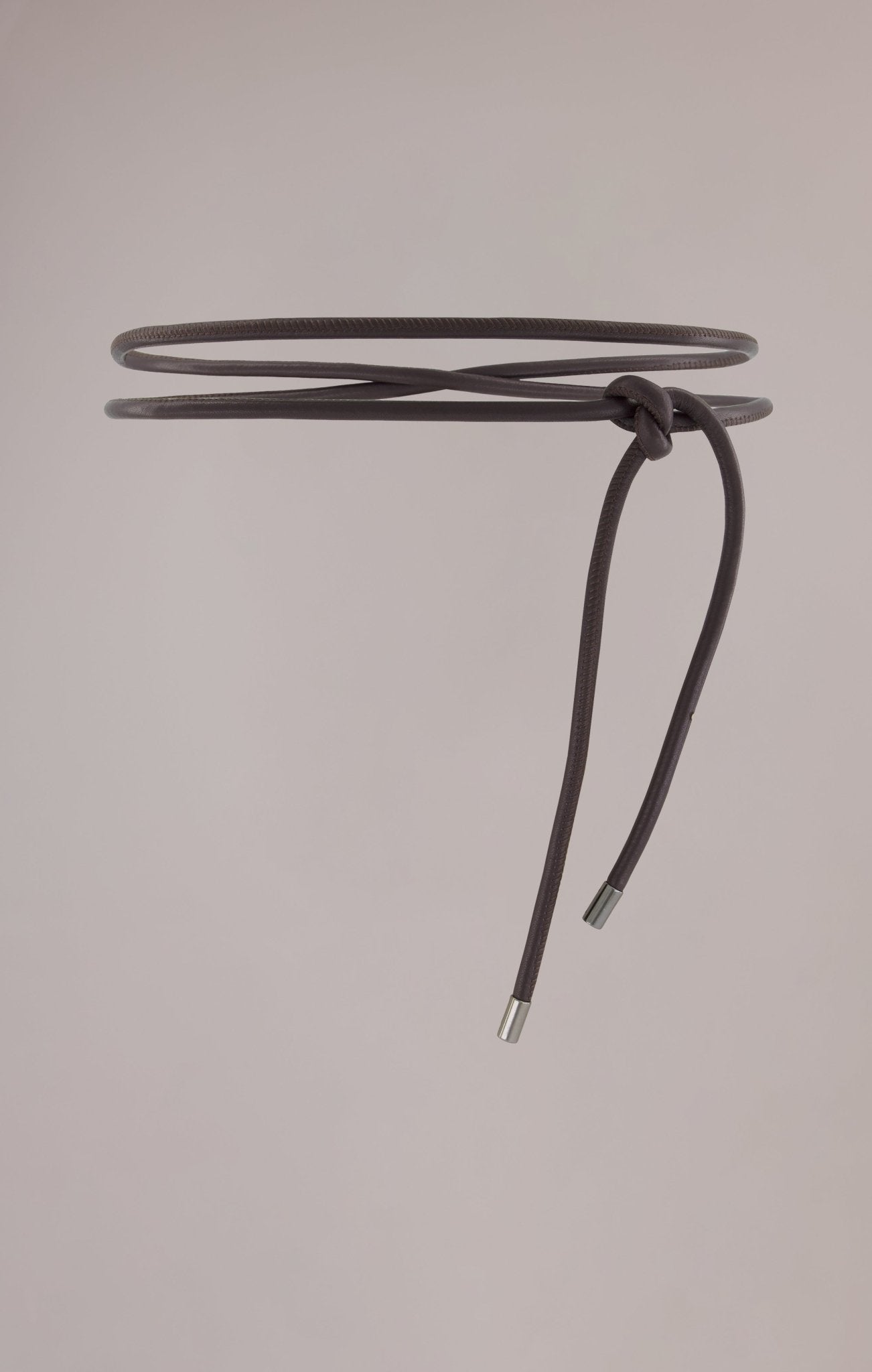 Bordeaux leather wrap belt made from soft, high-quality leather with whipstitch detailing and gunmetal metal cylinder ends. Designed to be wrapped and tied around the waist twice, this belt adds a chic touch to any outfit, perfect for accentuating your waist over jackets, shirts, or knitwear.