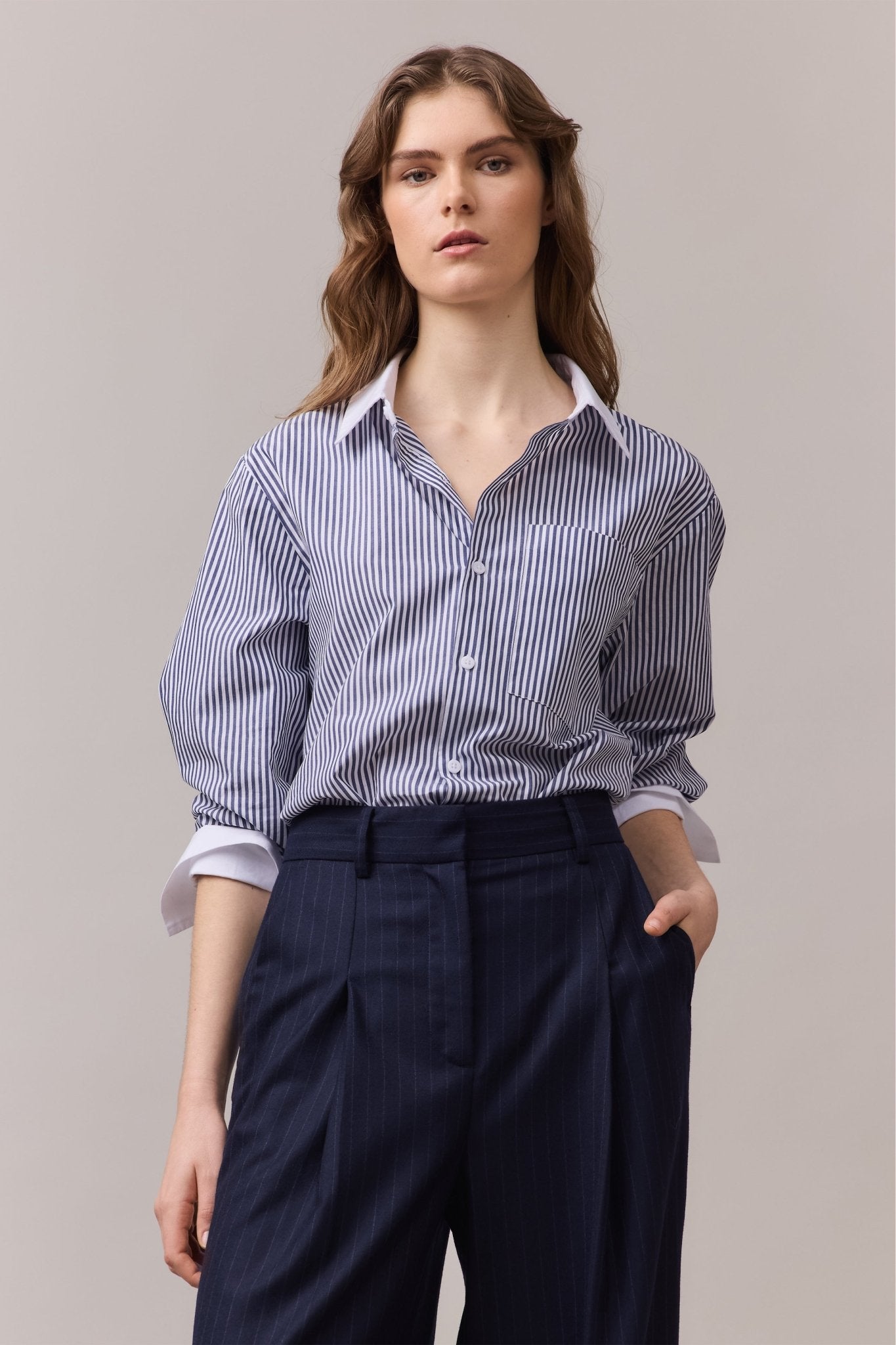 Woman wearing the Lenny Stripe Shirt in a casual fit, with a few buttons undone and sleeves rolled up. Paired with tailored navy trousers for a relaxed look.