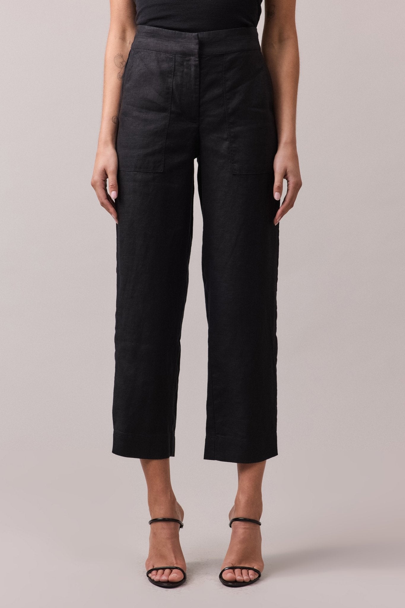 Front view of black slim-line 100% linen pants with a tailored waist and slight cropped length, styled with heels.
