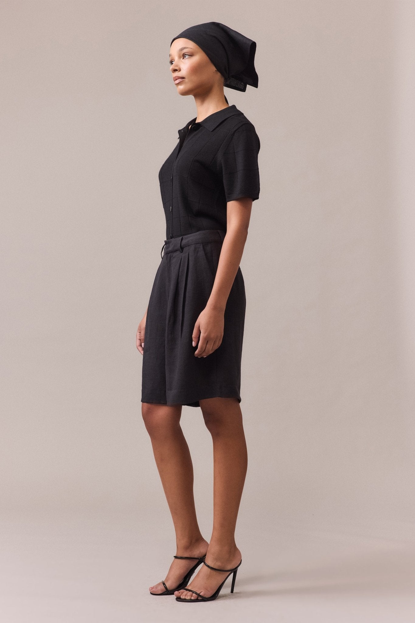 Side view of a woman wearing a black polo knit paired with black tailored shorts, highlighting the relaxed fit and textured grid stitch.