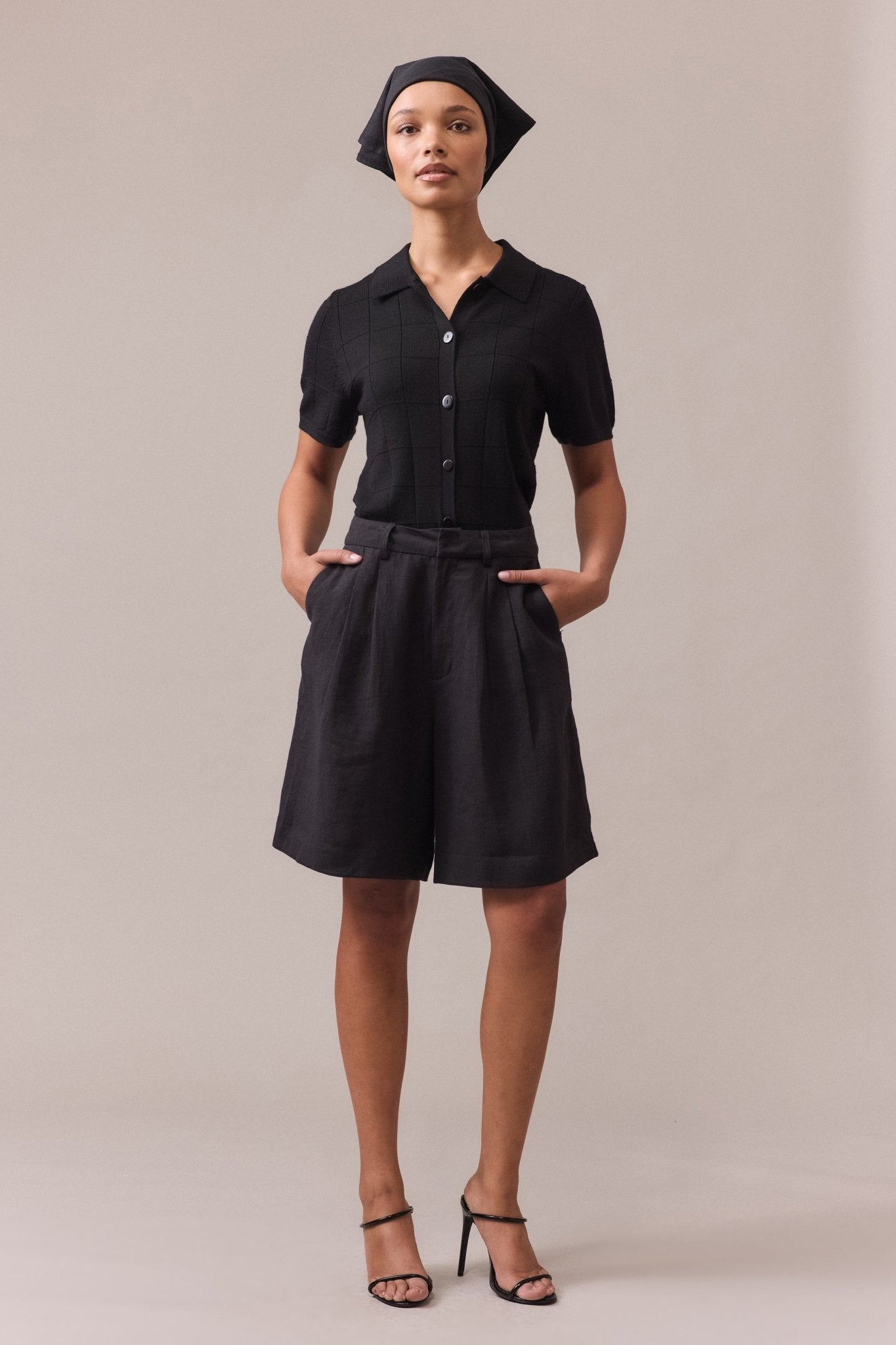 Woman wearing a black polo knit with hands in pockets, paired with black tailored shorts.