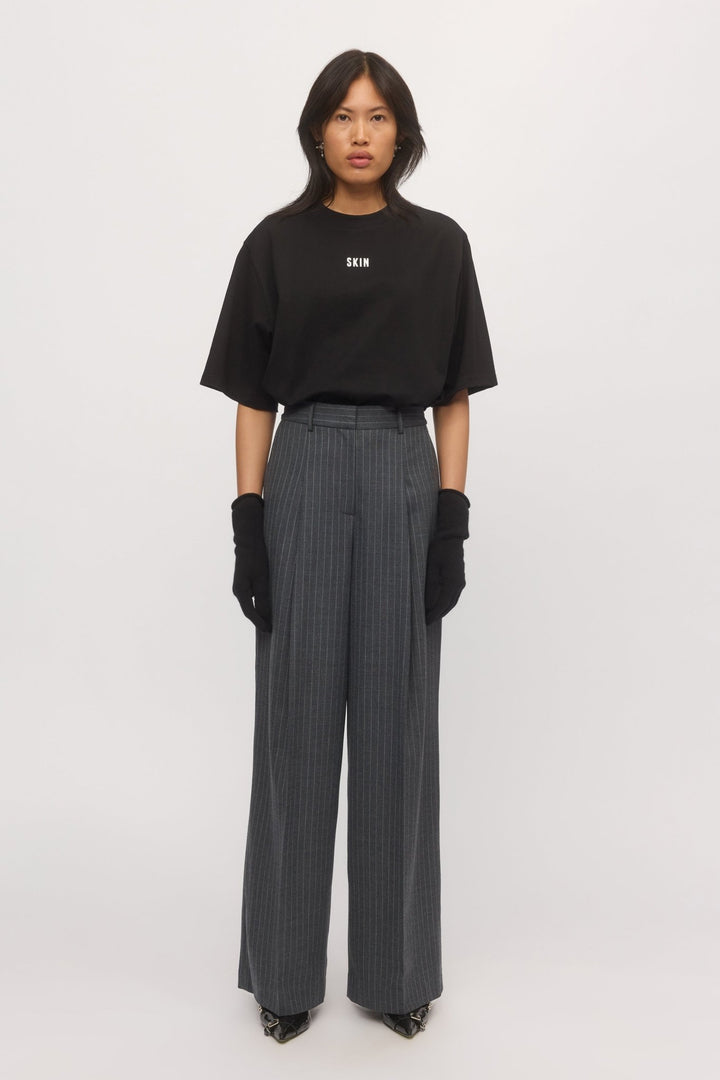A woman wearing graphite pinstripe Lola Wide Leg Pants styled with a black oversized SKIN t-shirt and black gloves. - Skin and Threads