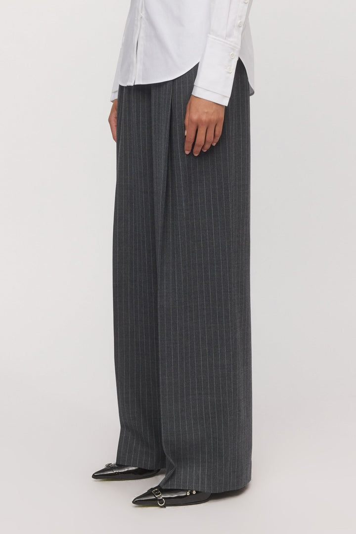 Side view of a woman wearing the Lola Wide Leg Pant in graphite pinstripe, paired with a white shirt and black pointed-toe flats. - Skin and Threads