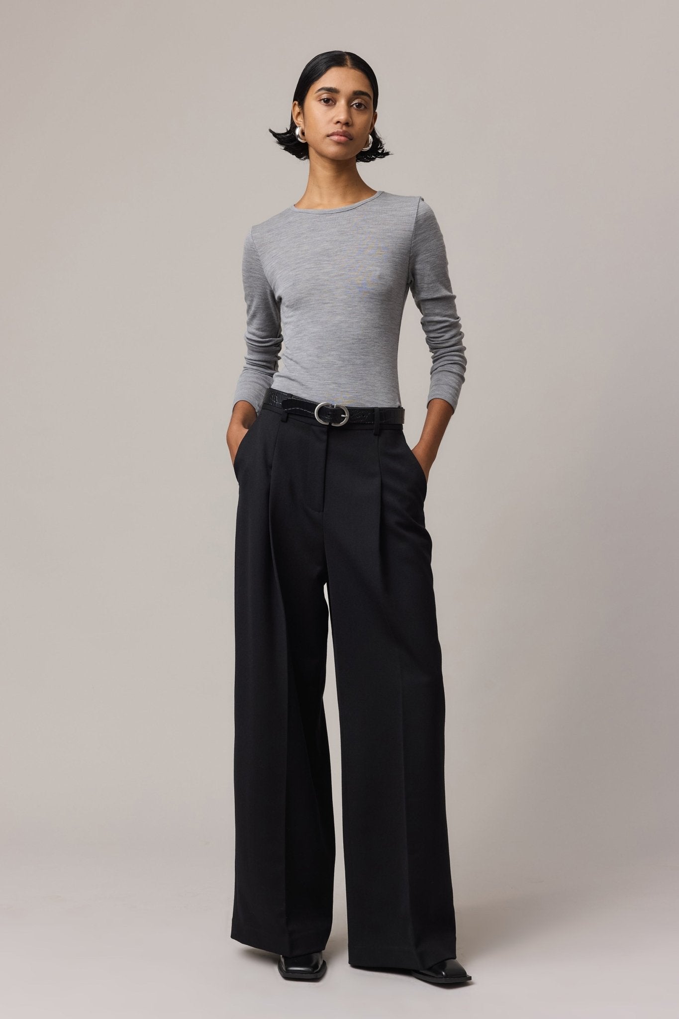 Woman wearing a long-sleeve Merino Wool Crew Neck in a classic crew neck fit, paired with black linen pants. She stands with her hands in the pockets.