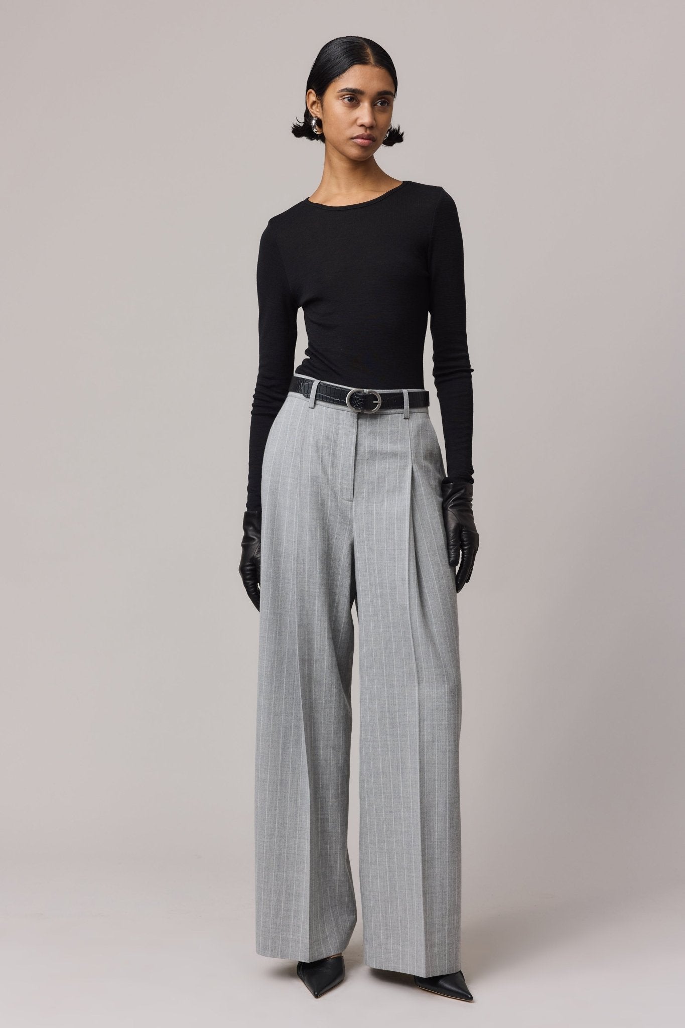 Woman wearing a black long sleeve Merino Wool Crew Neck with a crew neckline, paired with grey long pants. The top is made from 100% fine Australian Merino wool, offering a soft, temperature-regulating fit.
