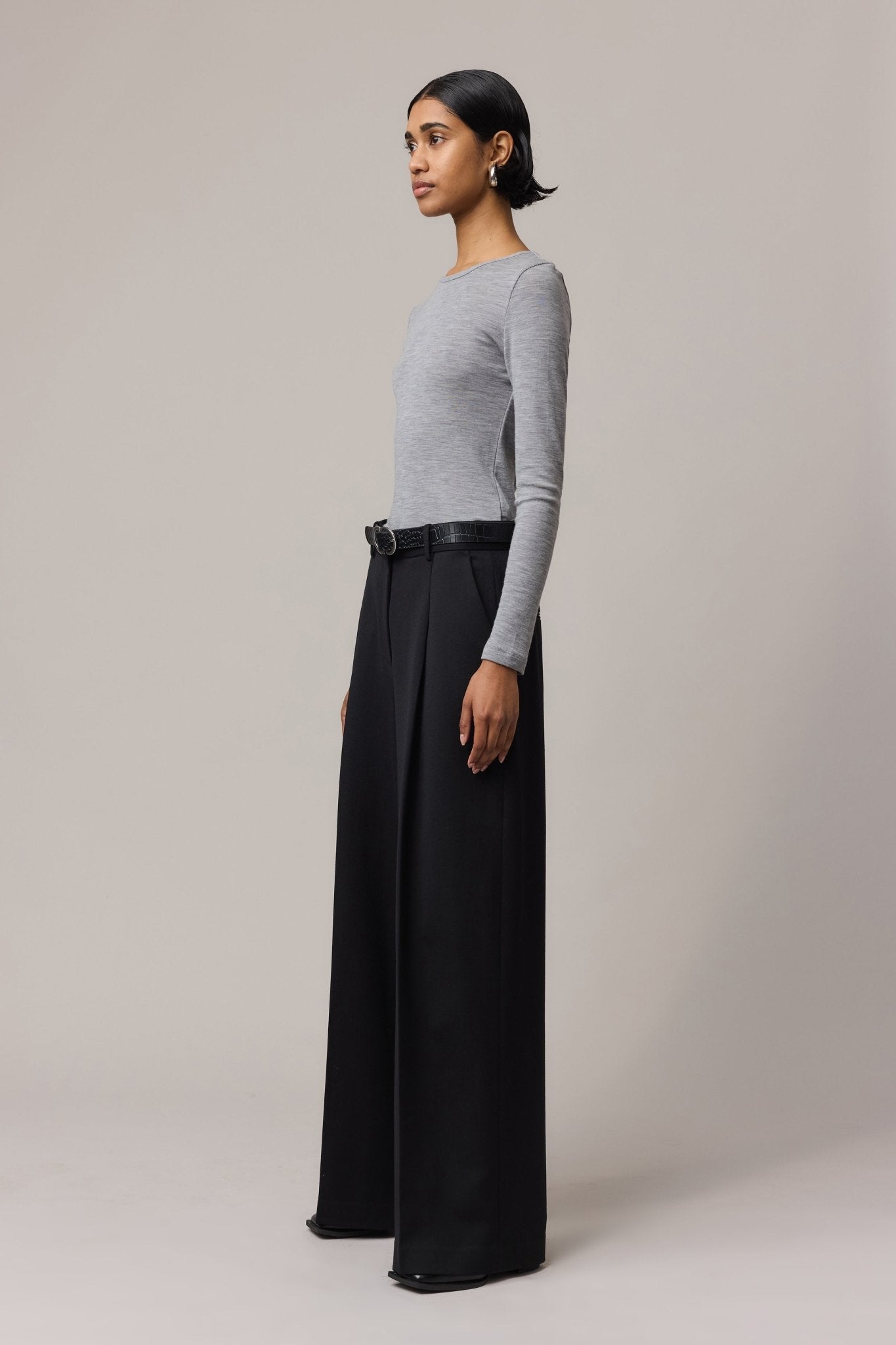 Side view of a woman wearing a long-sleeve Merino Wool Crew Neck with black linen pants.