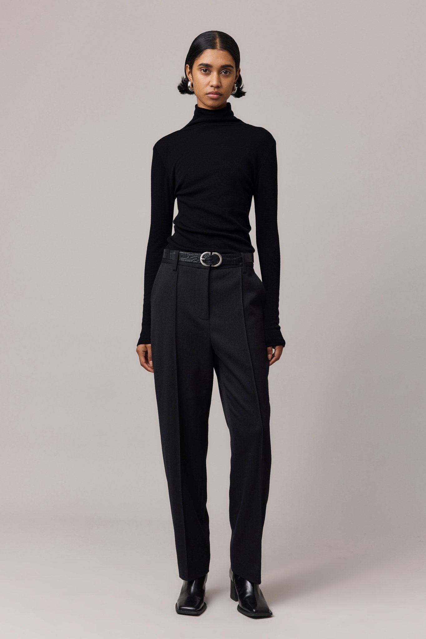 Woman styled in a black 100% Merino Wool Slim Fit Skivvy paired with sleek black pants. This cozy skivvy features a classic fitted neckline, offering both elegance and warmth.