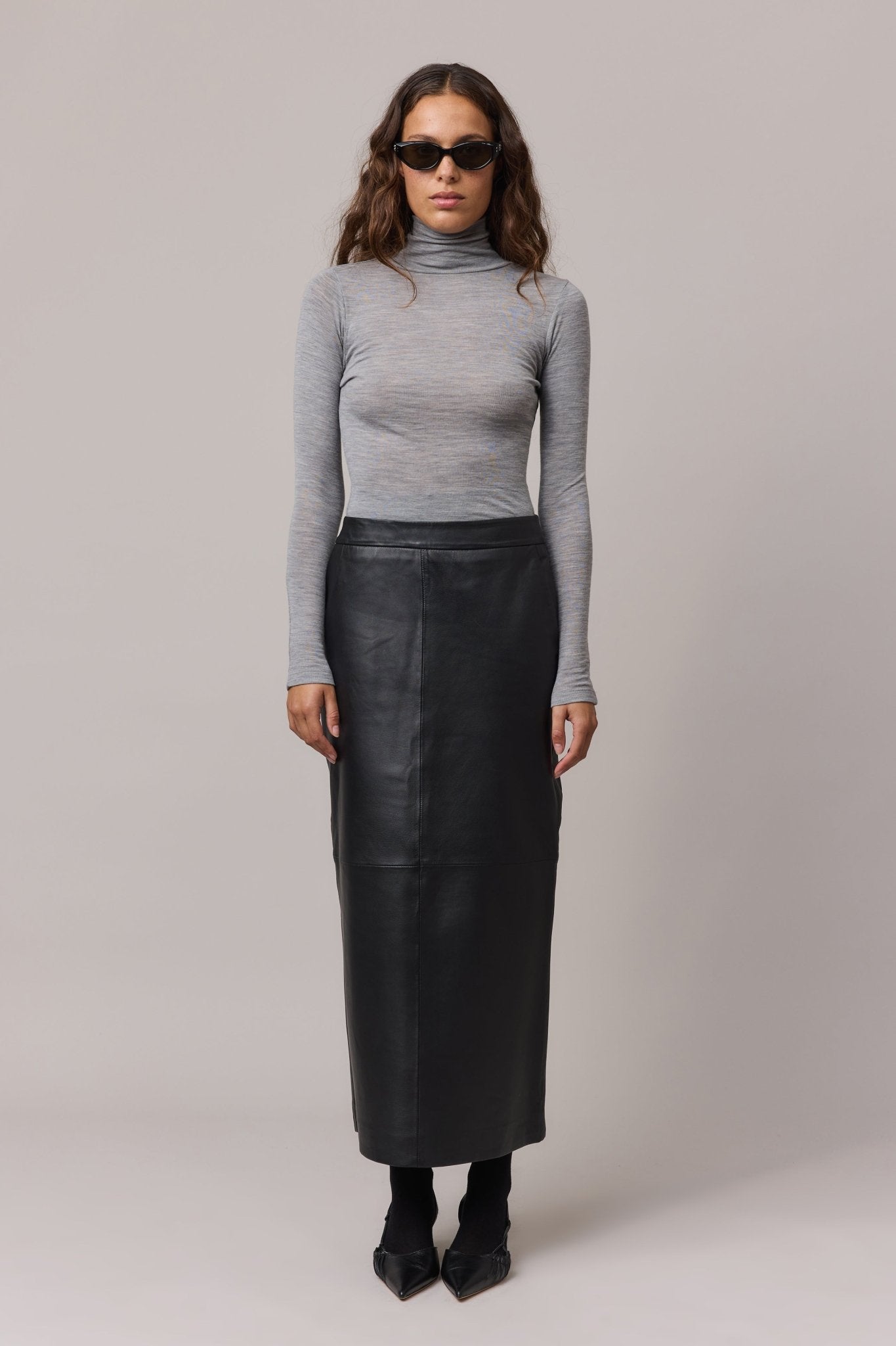 Woman wearing a grey 100% Merino Wool Slim Fit Skivvy paired with a long leather maxi skirt. The skivvy features a classic fitted neckline offering warmth and style.