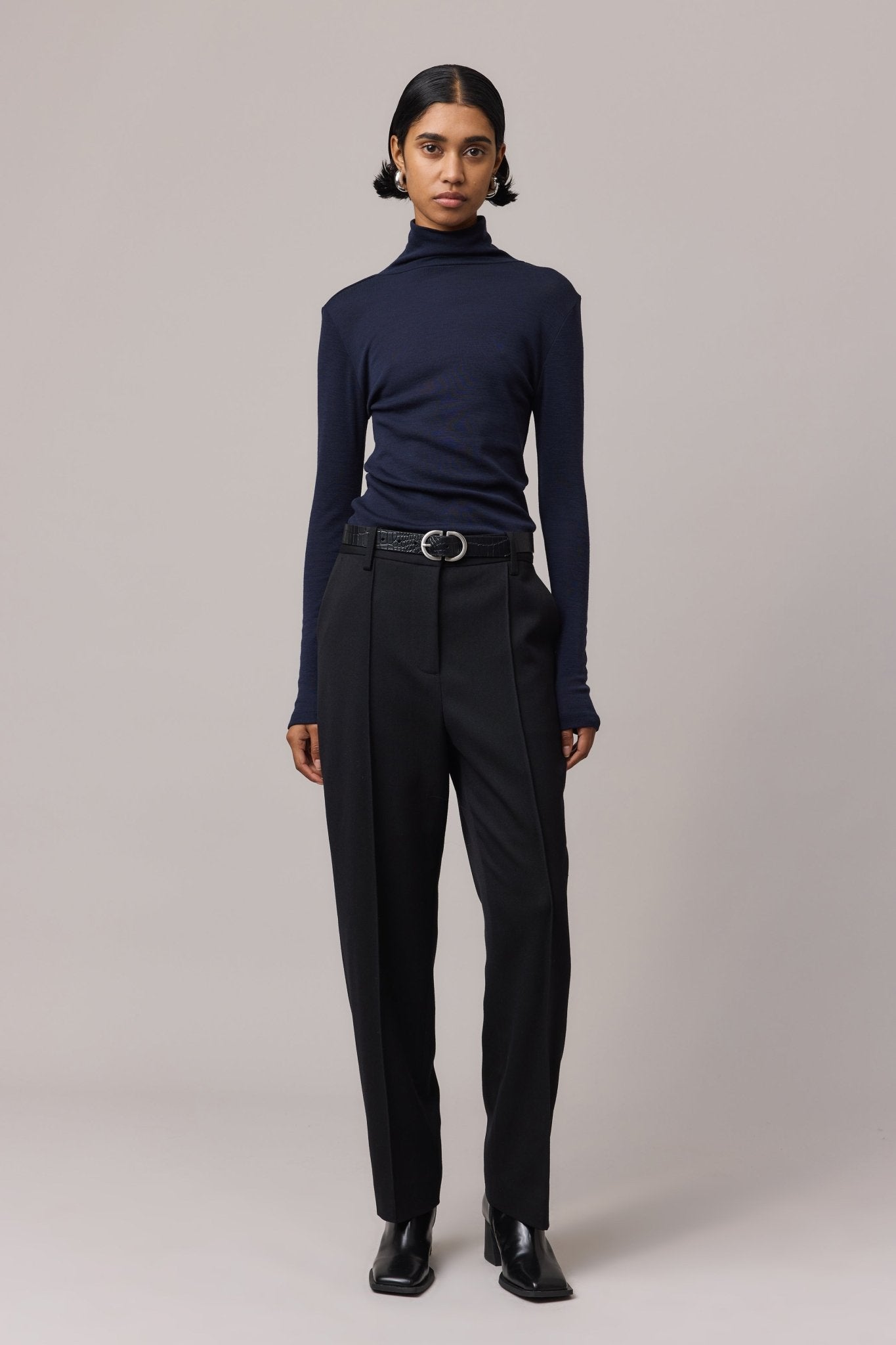 Woman wearing an indigo 100% Merino Wool Slim Fit Skivvy paired with black pants. The skivvy features a classic fitted neckline, designed for warmth and layering.