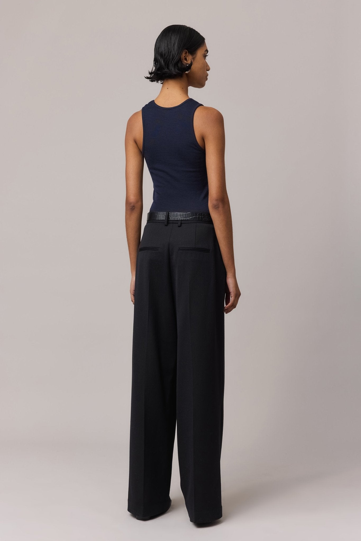 Woman seen from the side wearing an indigo Merino Wool Tank Top with a fitted crew neckline, paired with black wide-leg pants