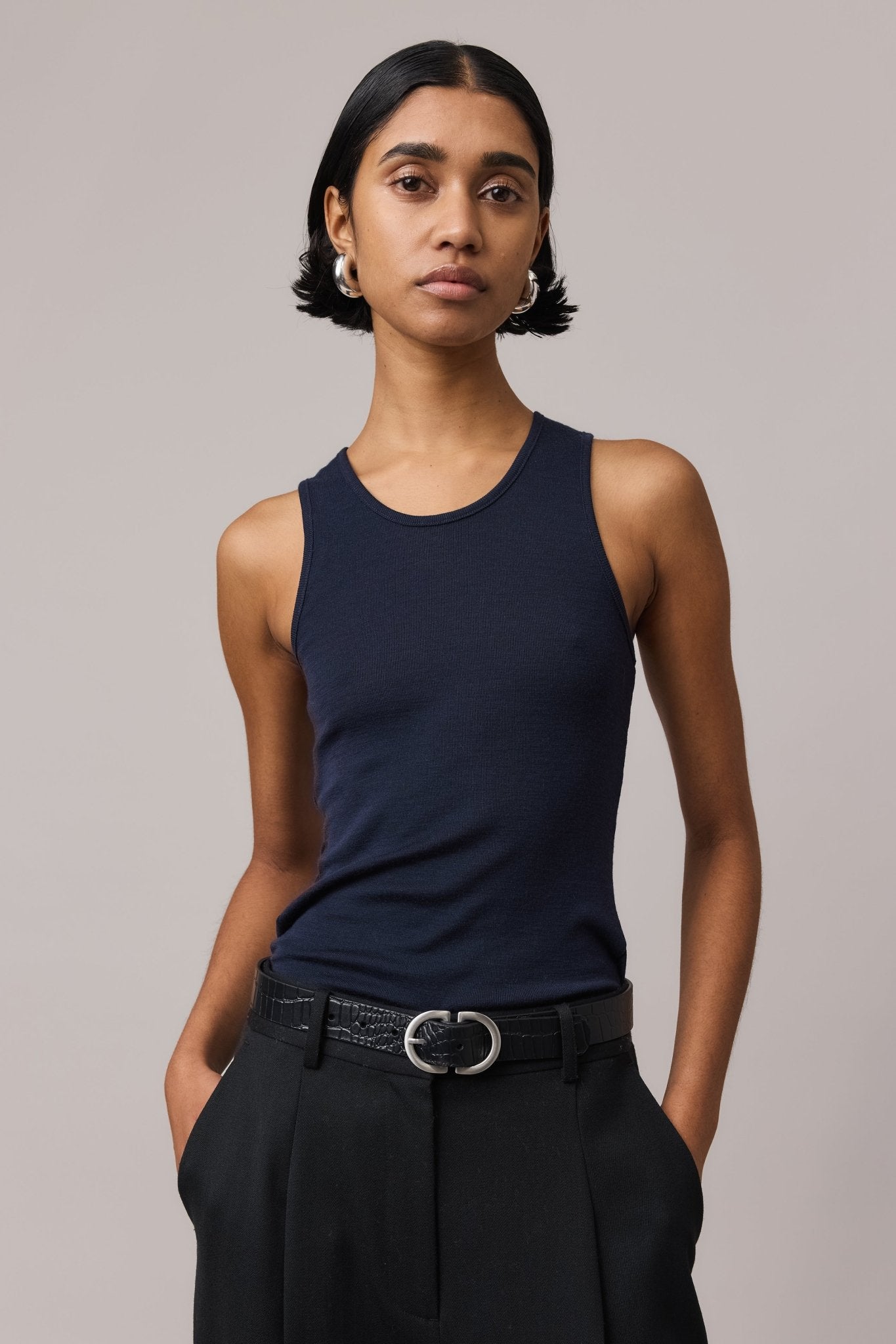 Woman wearing an indigo Merino Wool Tank Top with a fitted crew neckline, paired with black pants.