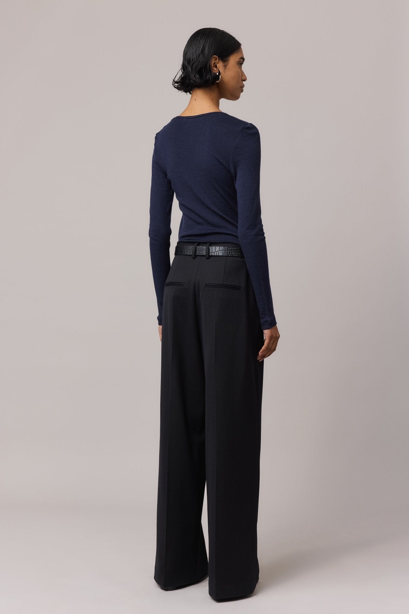 View from behind of a woman wearing an indigo Merino Wool V Neck Top with black wide-leg pants.