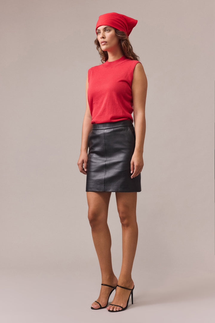 Side profile of a woman in a red cotton knit top, black leather skirt, and red headscarf, showing the body-skimming fit and ribbed side panel detail.
