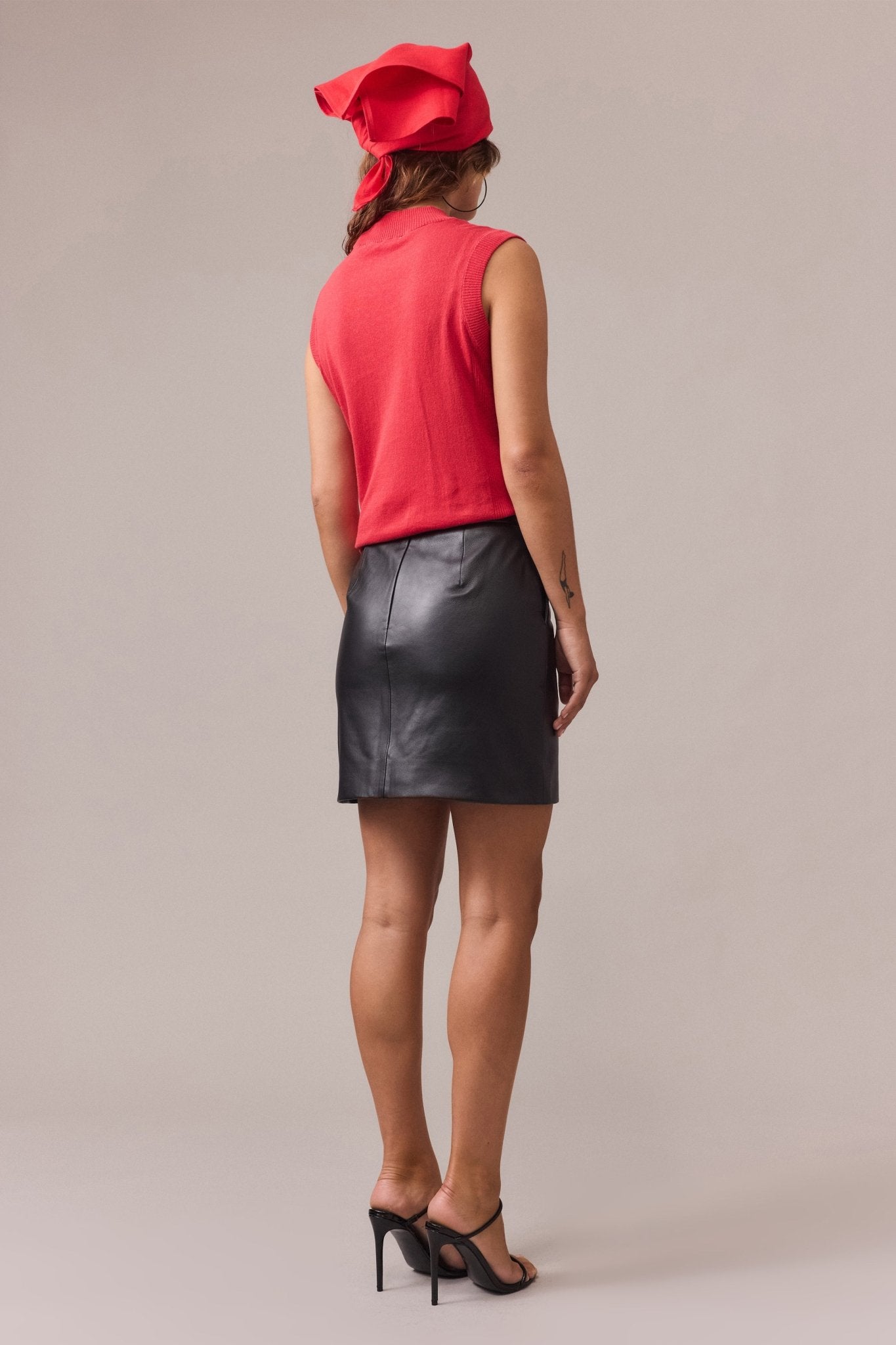 Back view of a red sleeveless knit top featuring rib trim at the armholes and a seamless fitted silhouette, paired with a black leather skirt.