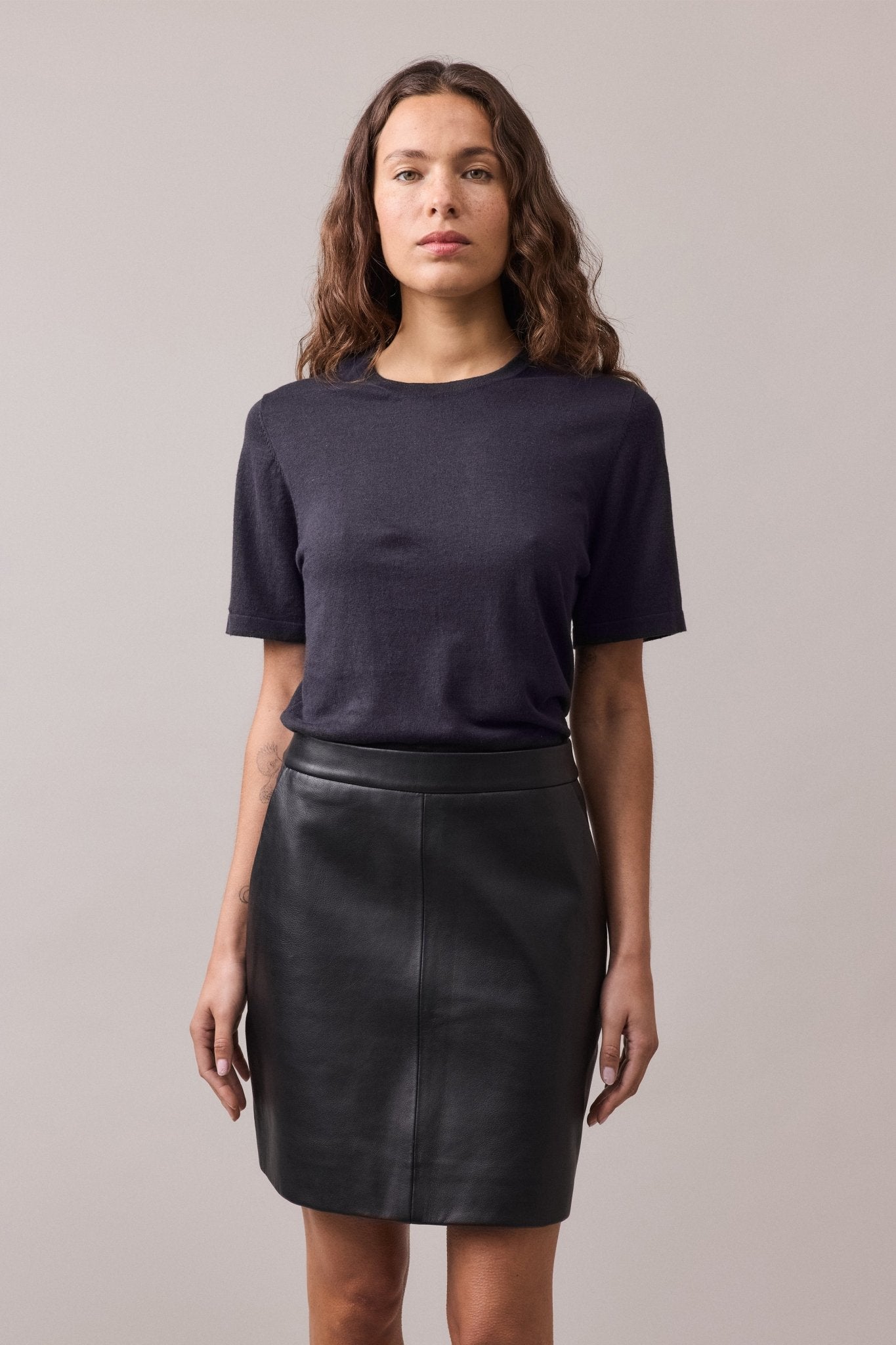 Close-up view of the navy Nara Knit Tee, highlighting the fine ribbed collar, hem, and cuffs. The linked knitwear seams and relaxed fit of the shirt are also visible.