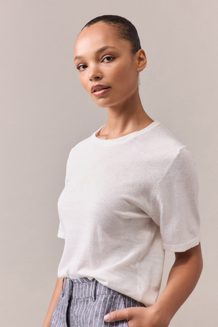 Close-up of the white Nara Knit Tee, showcasing the fine ribbed collar and short sleeves. The soft hemp and cotton blend fabric is highlighted, emphasizing the relaxed fit and linked knitwear seams.