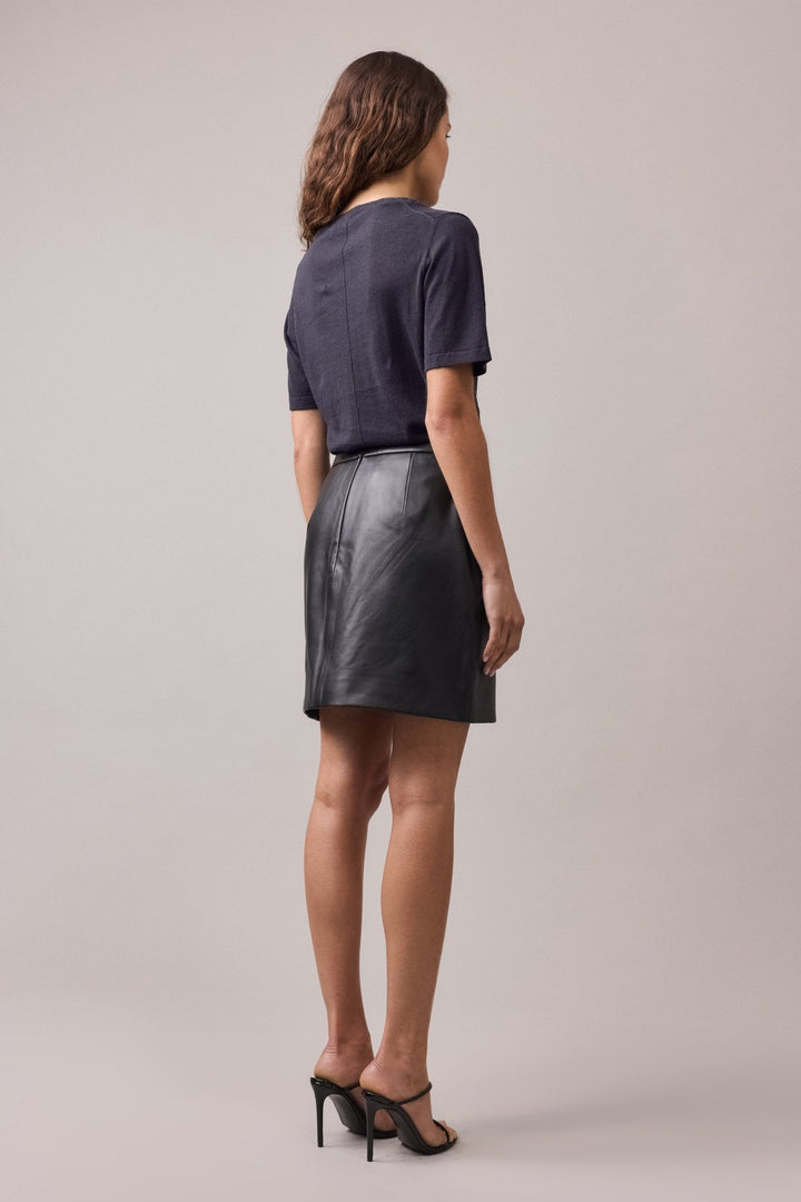 View of the woman from behind, wearing the navy Nara Knit Tee tucked into a mini leather skirt.