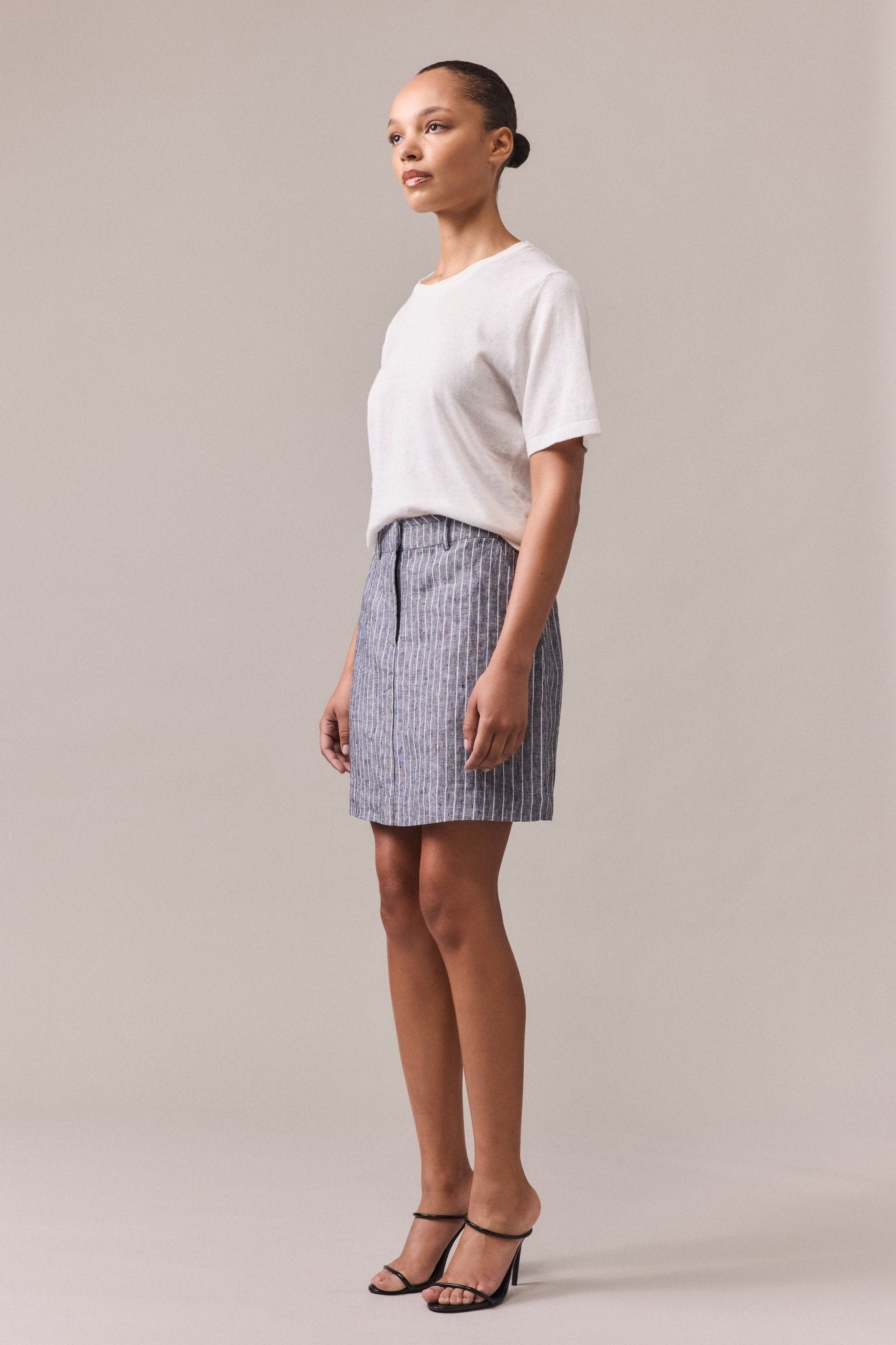 Woman wearing the Nara Knit Tee tucked into a grey mini skirt with white lines. The soft hemp and cotton blend tee features a relaxed fit, fine ribbed hem, collar, and cuffs, with linked knitwear seams.