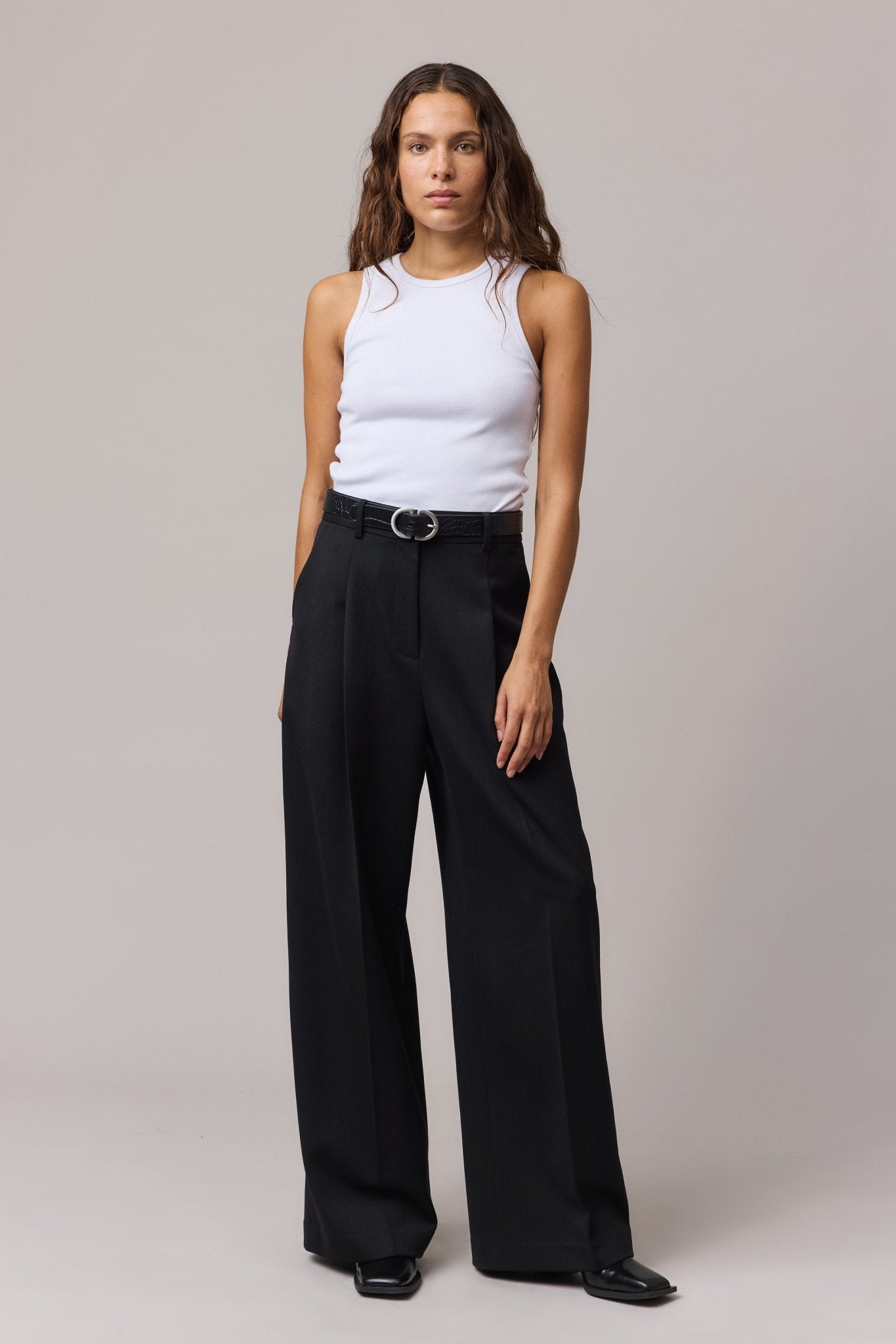 Woman wearing a white organic cotton rib tank top with a round neck, paired with black high-waisted trousers.