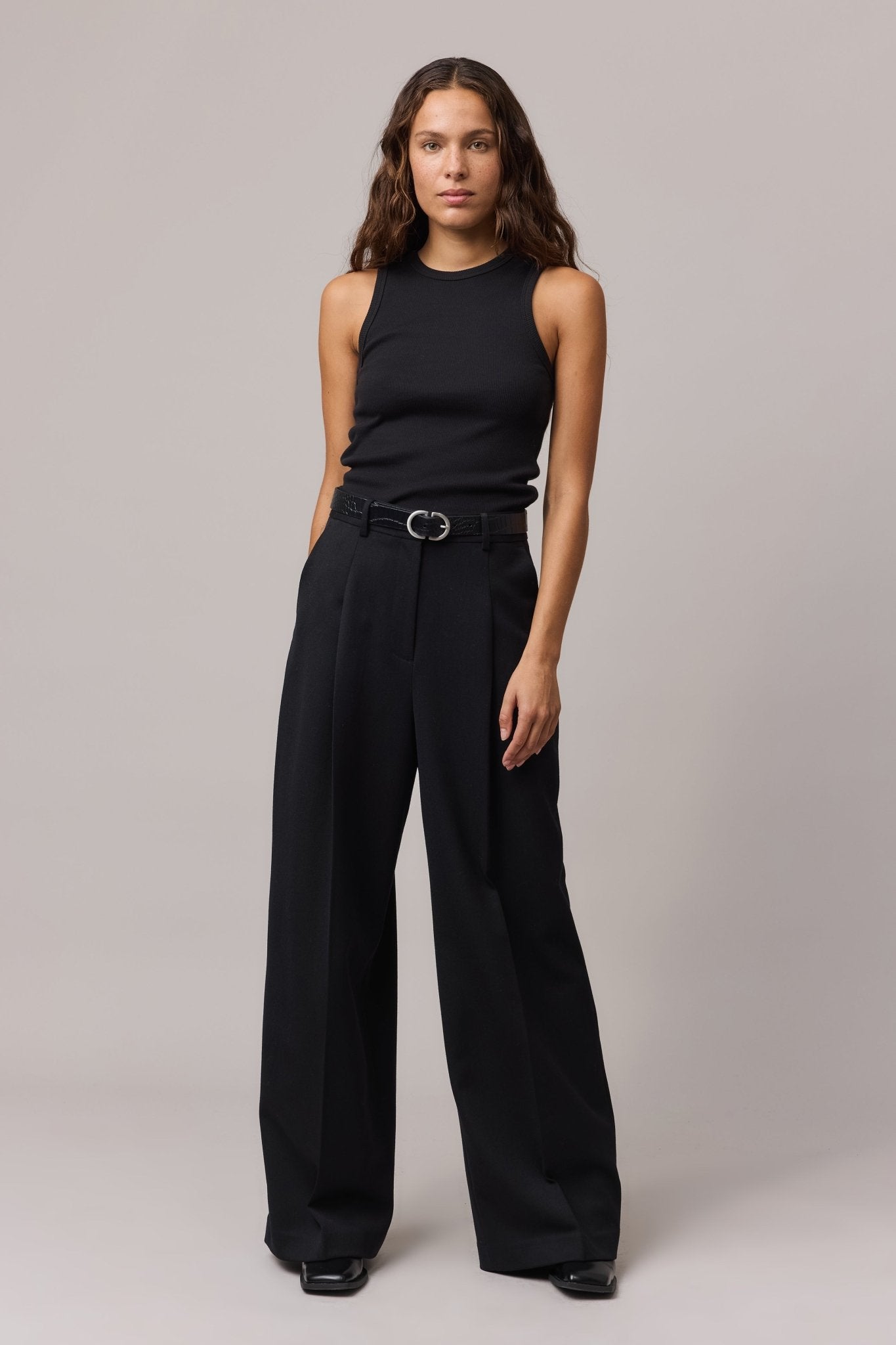 Full-body view of the woman in the black cotton tank top and wide-leg black trousers, styled with a black belt.