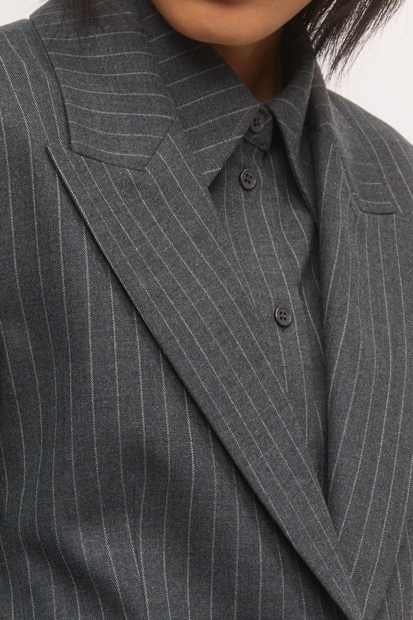 Close-up of the Single Button Blazer in graphite stripe, showcasing the tailored lapel, pinstripe wool texture, and sharp collar detailing layered over a matching shirt.