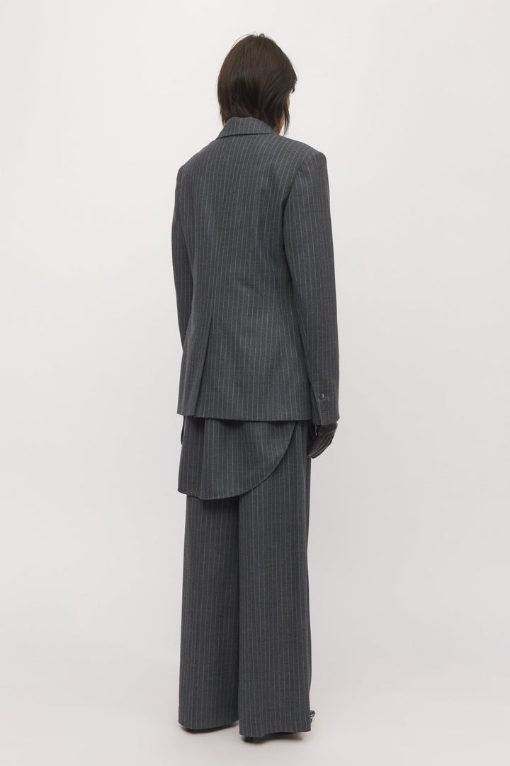 Back view of a woman in a graphite pinstripe blazer and shirt, highlighting the classic tailoring and long-line silhouette.