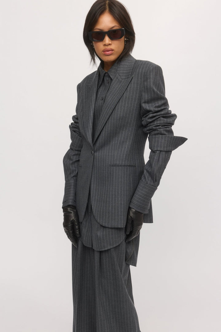 Woman wearing the graphite stripe Single Button Blazer styled with matching trousers, sleeves ruched at the elbows, paired with leather gloves and sunglasses for a structured, confident look.