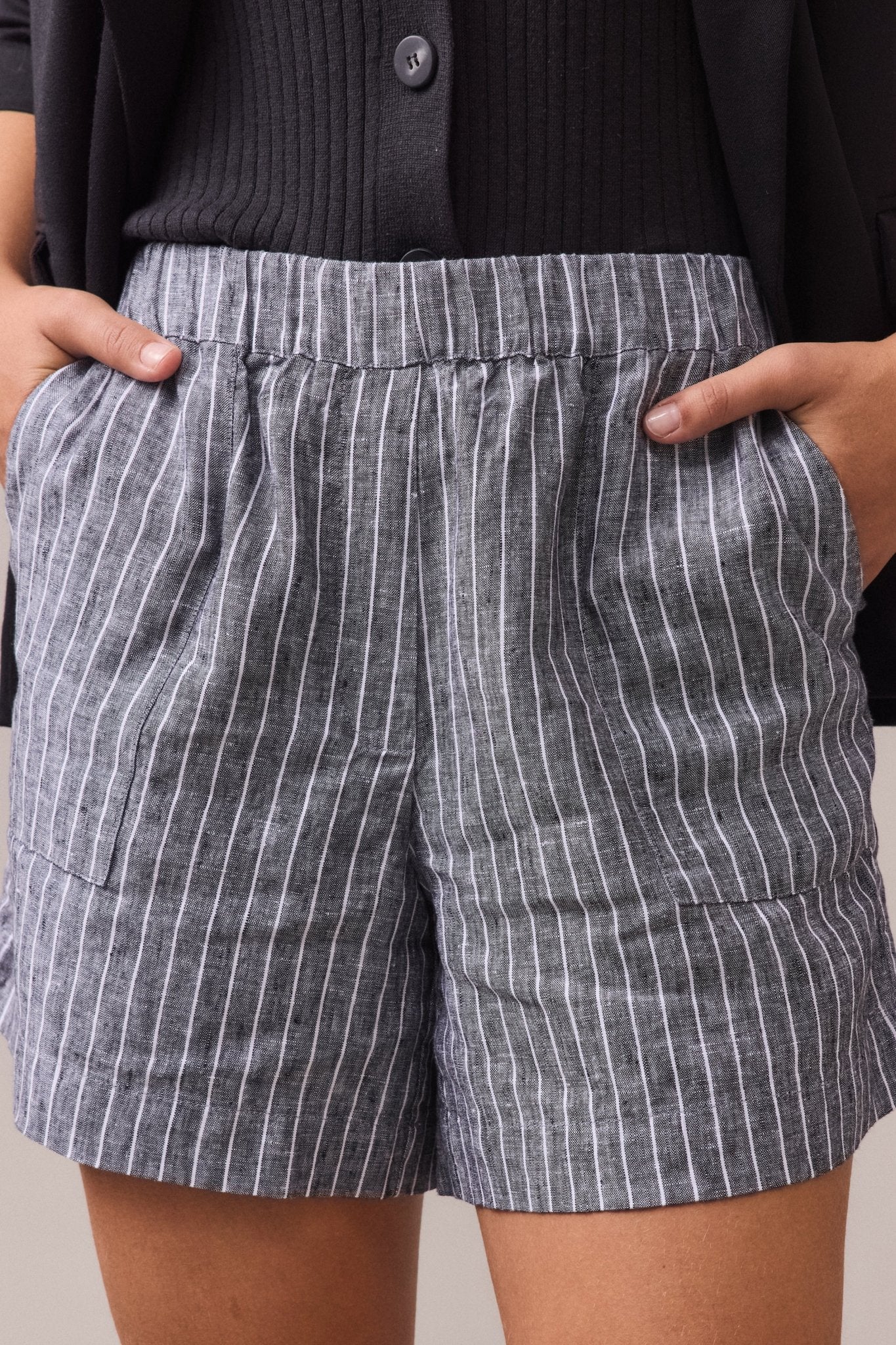 Woman wearing Soma Linen Shorts with a gray and white pinstripe pattern, hands casually tucked into the pockets.